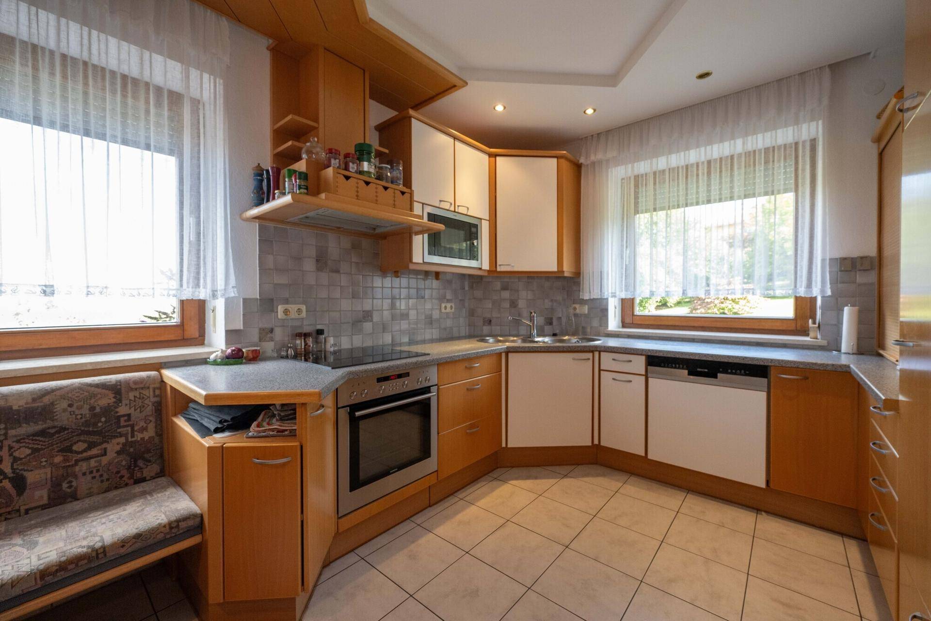 Funktionale Küche mit Holzschränken, Fliesenboden und integrierten Geräten.