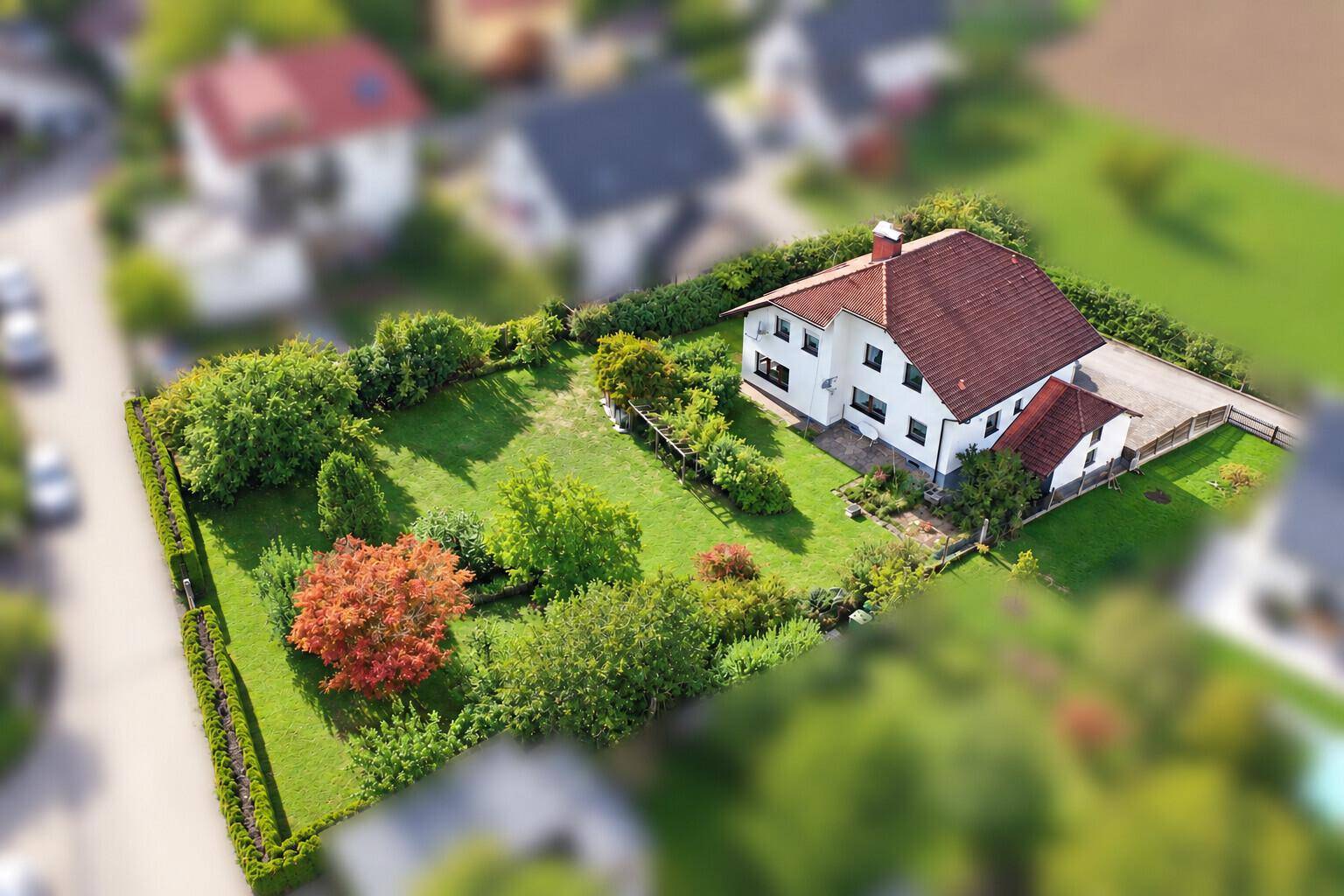 Weitläufige Luftaufnahme eines Einfamilienhauses mit großem, grünem Garten und altem Baumbestand.