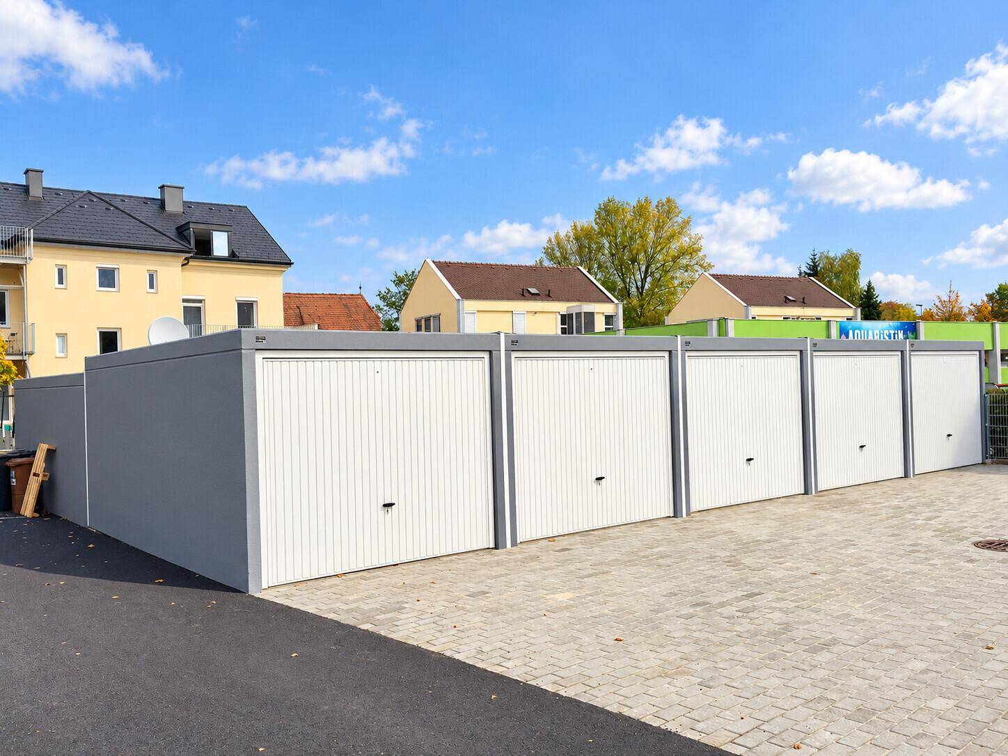 Nahaufnahme einer Reihe moderner Garagenboxen mit weißen Sektionaltoren und grauen Wänden.