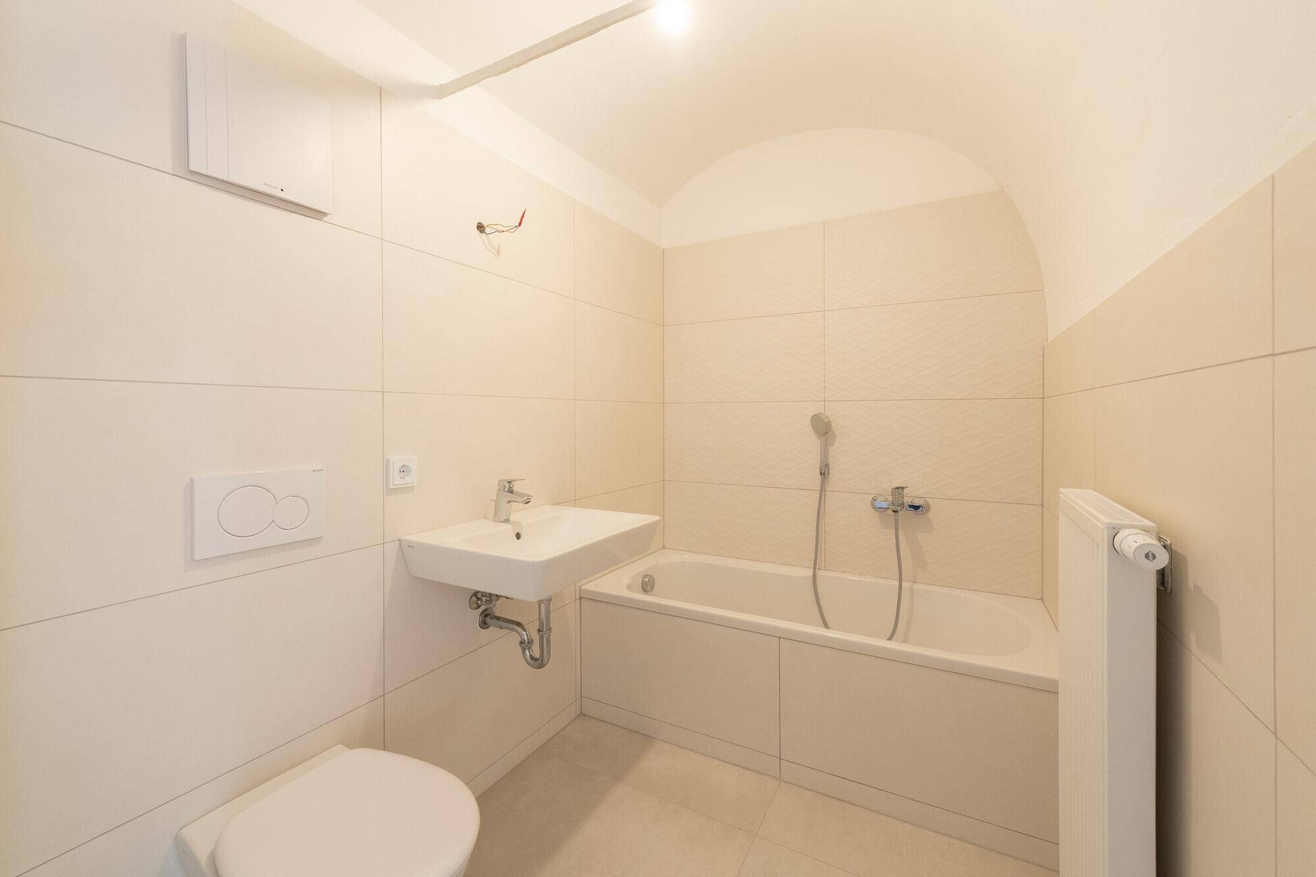 Helles Badezimmer mit Badewanne, WC und Waschbecken, gefliest in warmen Beigetönen.