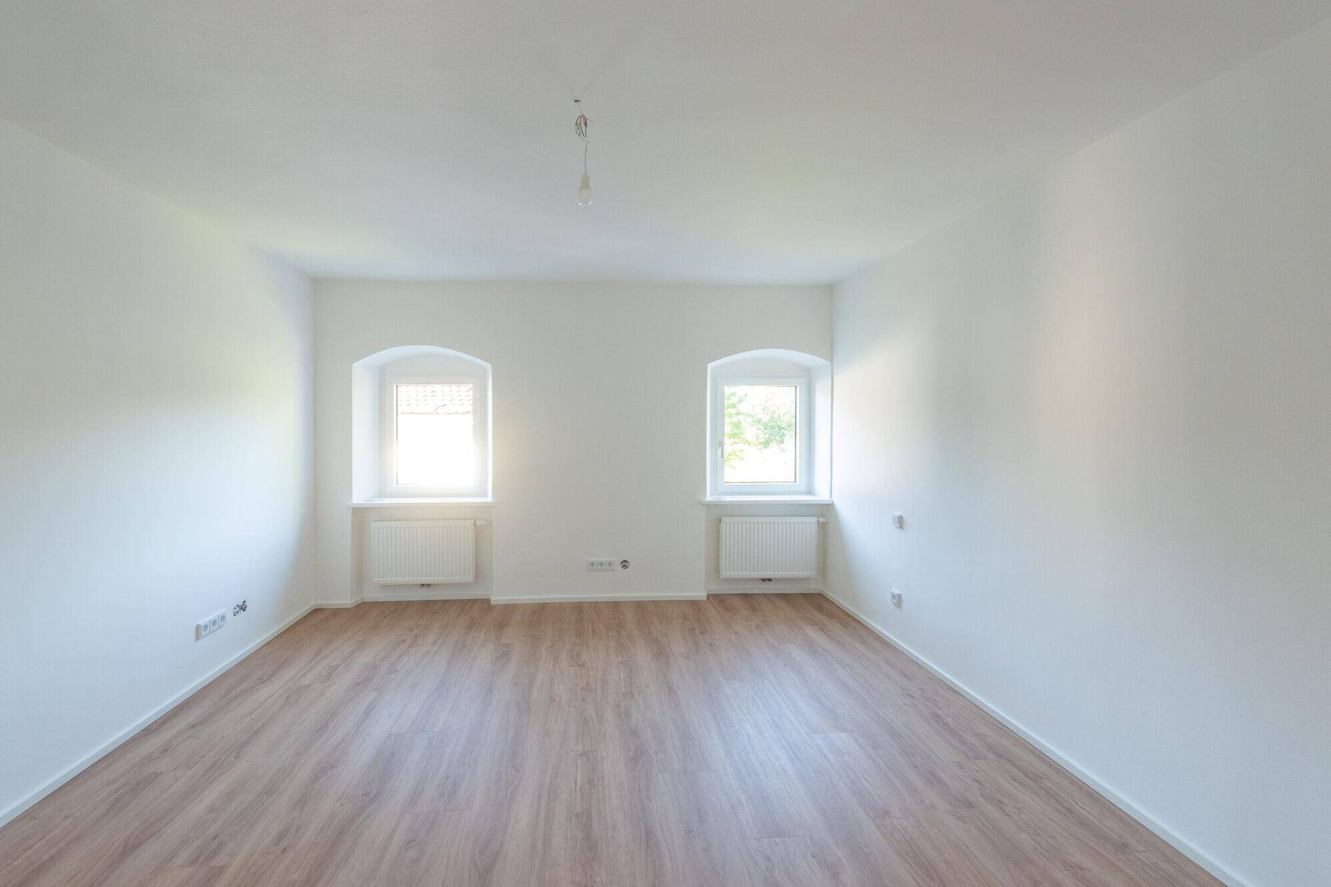 Lichtdurchfluteter Raum mit zwei Fenstern, Laminatboden und frisch gestrichenen weißen Wänden.