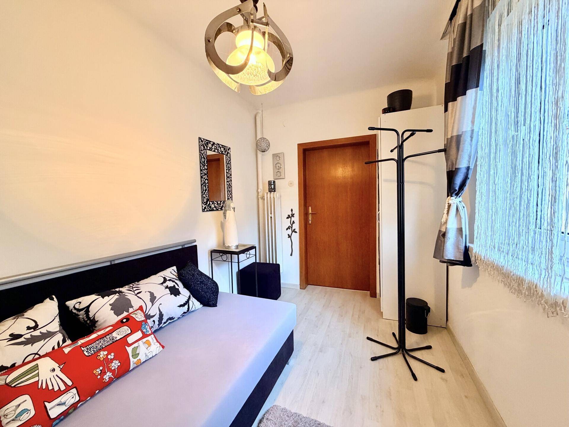 Schlafzimmer mit Tagesbett, Garderobe und Zugang zu einem weiteren Raum.