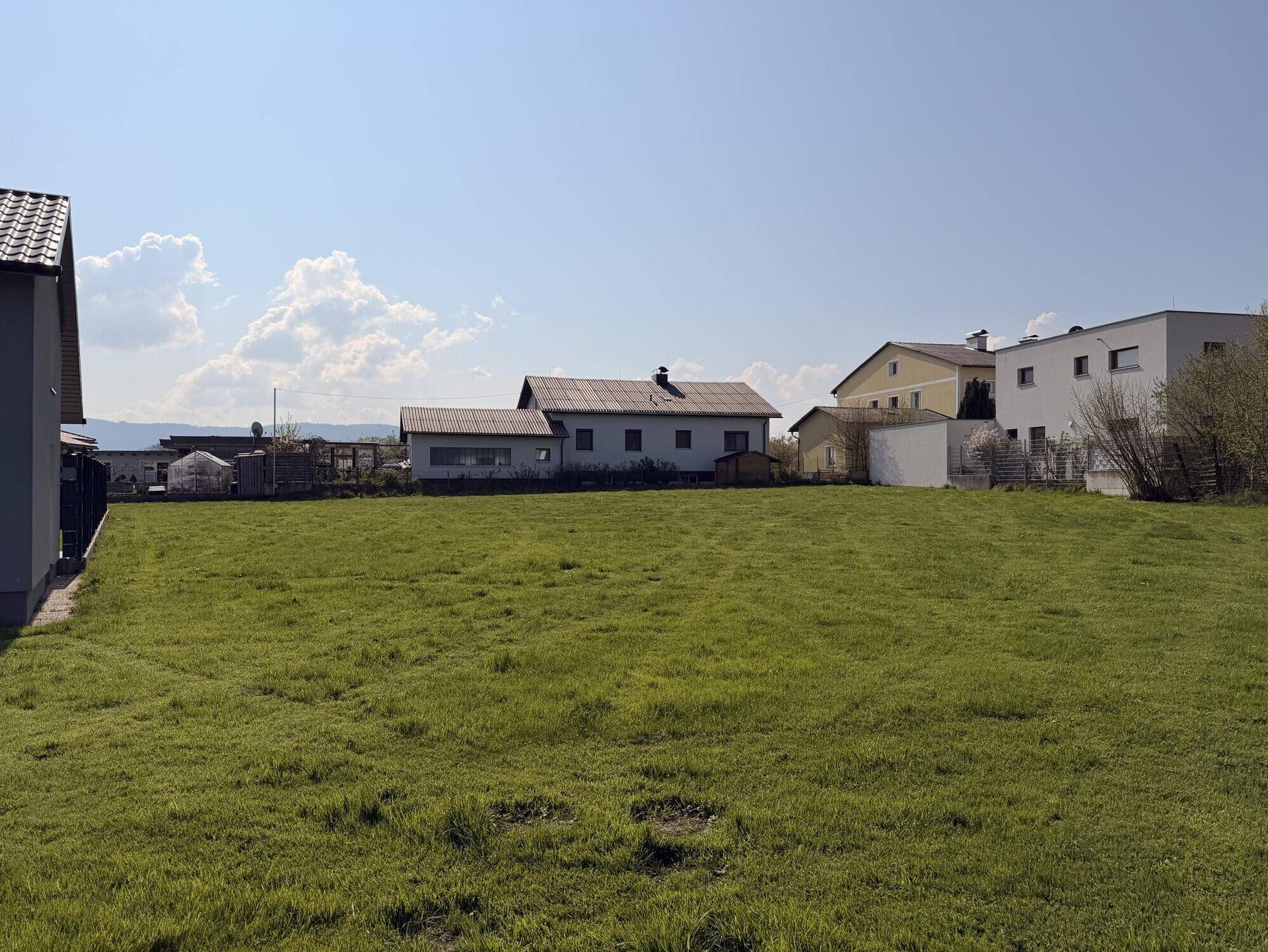 Sonniges, grünes Grundstück mit verschiedenen Häusern in der Nachbarschaft und leicht bewölktem Himmel.