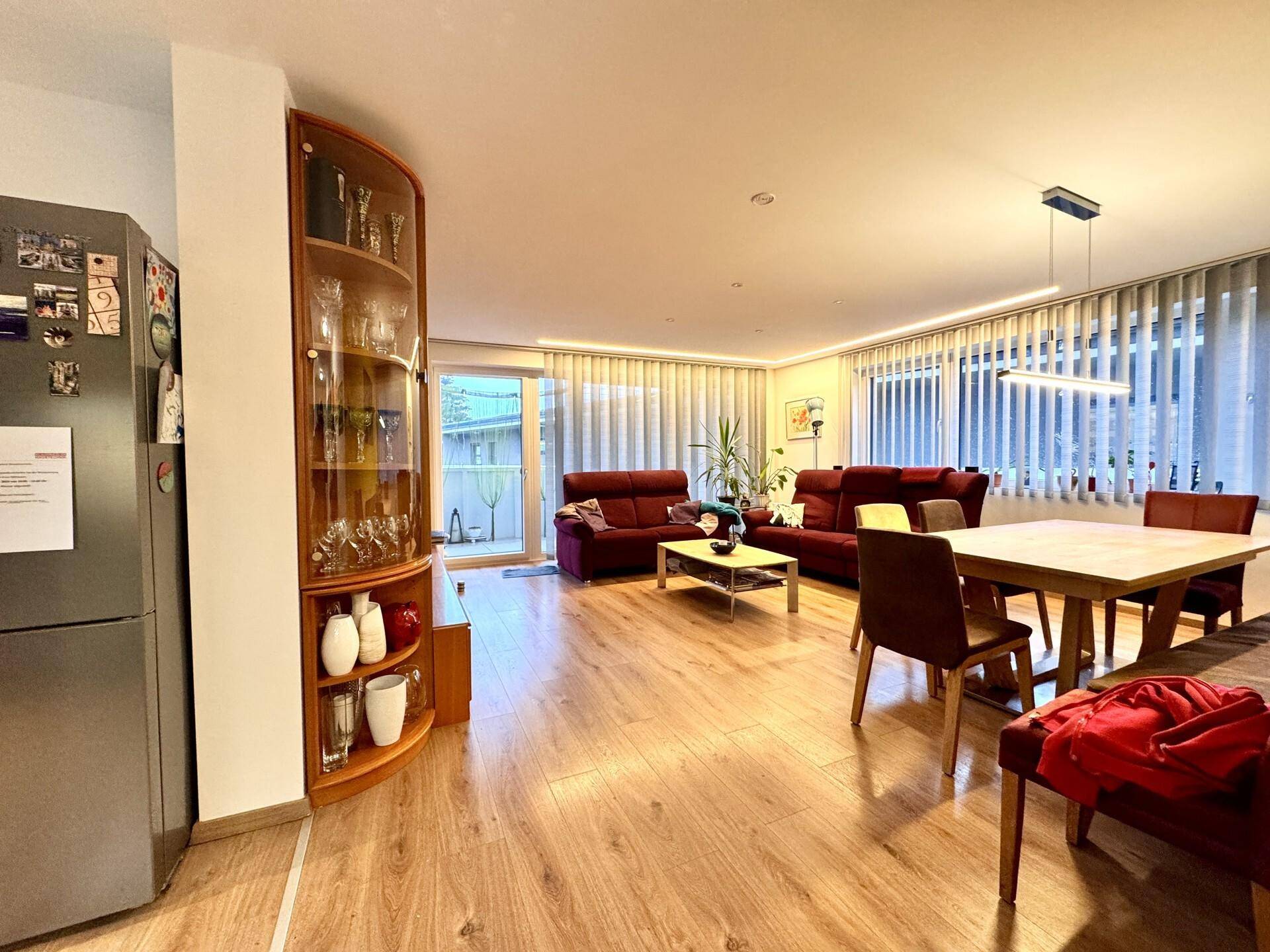 Geräumiger Wohn-Essbereich mit Holzboden, bequemen Sofas und Zugang zu einem Balkon.