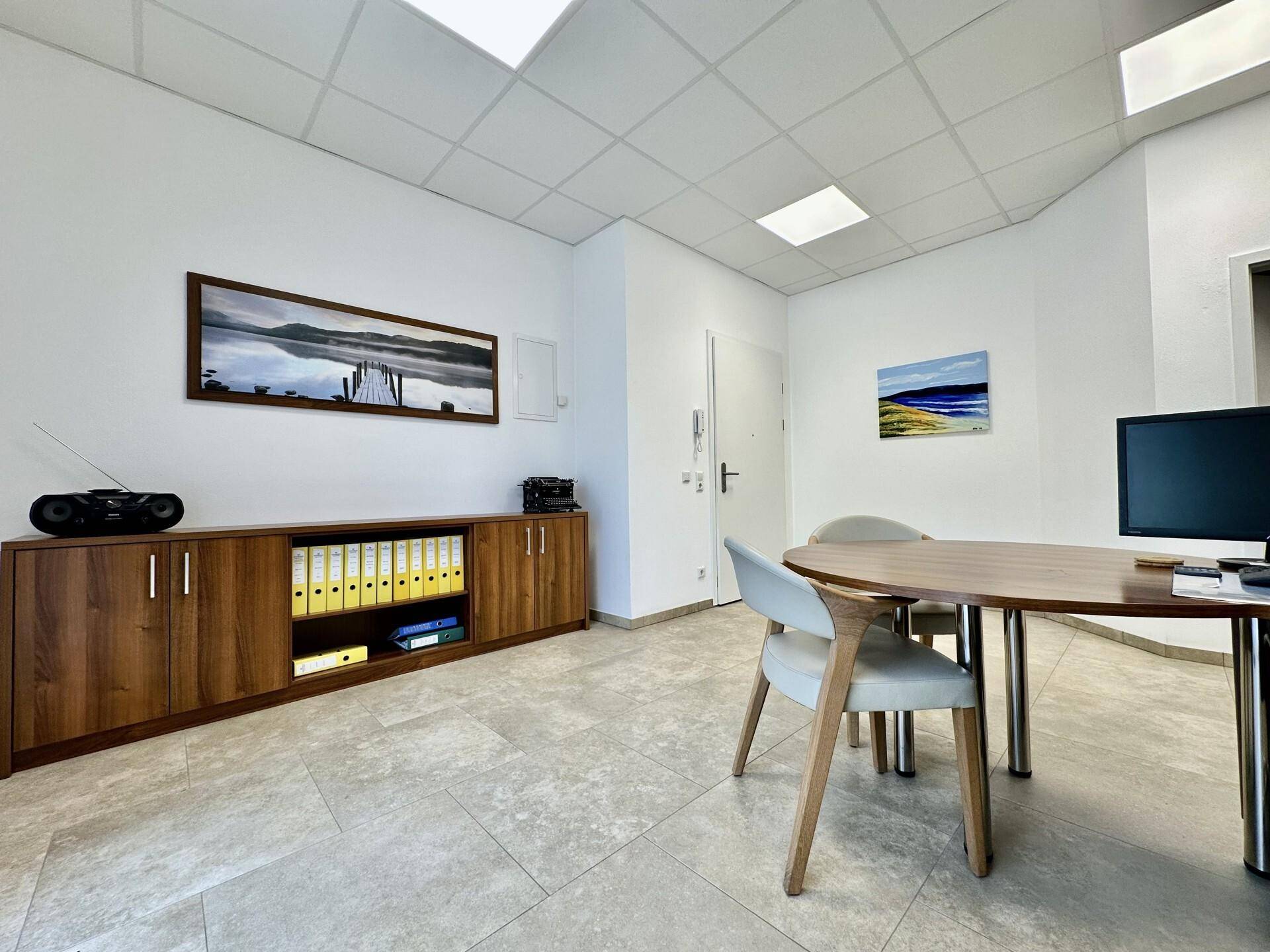 Helles Büro mit einem langen Holzschrank, einem runden Besprechungstisch und einem modernen Fliesenboden.