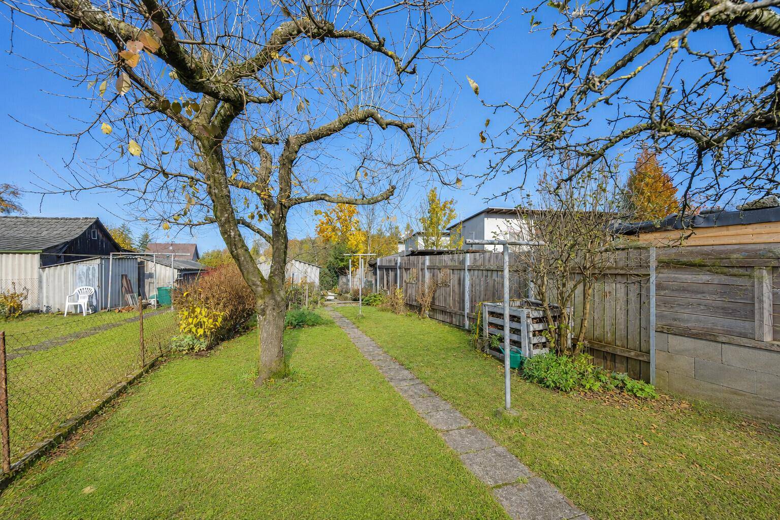 Langer Garten mit Rasenfläche, alten Bäumen und Holzzaun im hinteren Bereich.