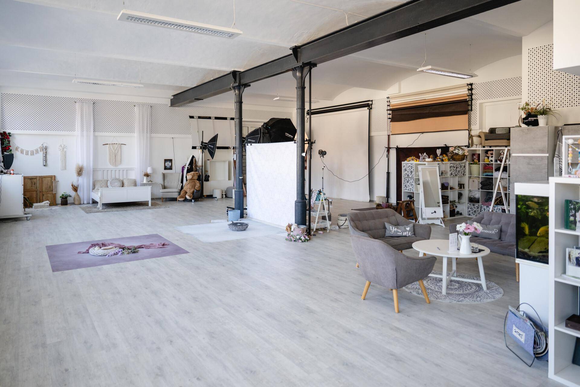 Geräumiges Fotostudio mit verschiedenen Kulissen, Sitzbereichen und professioneller Beleuchtungsausrüstung.
