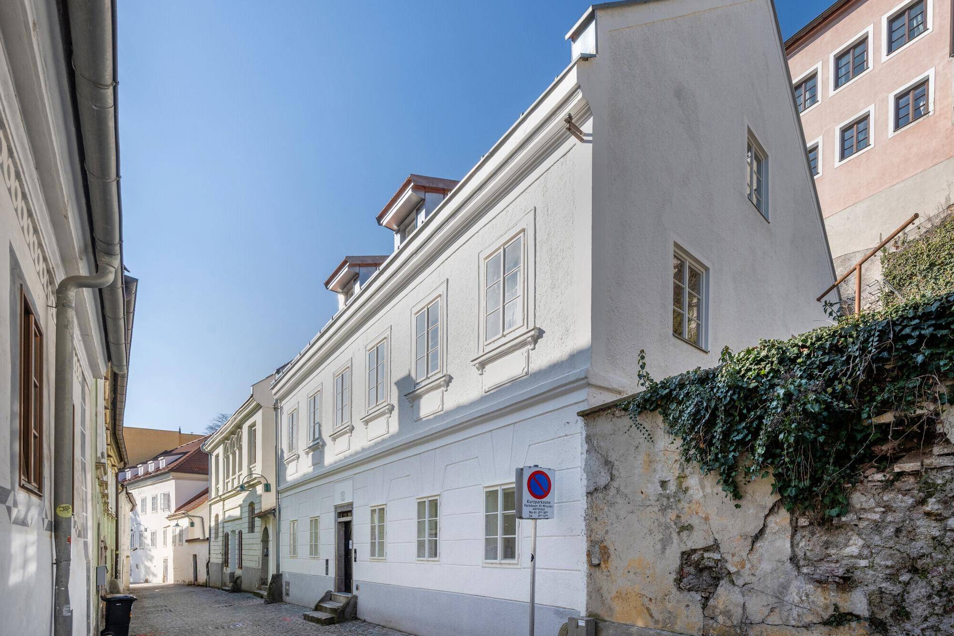 Historisches Gebäude in einer ruhigen Gasse mit traditioneller Architektur und weißer Fassade unter blauem Himmel.