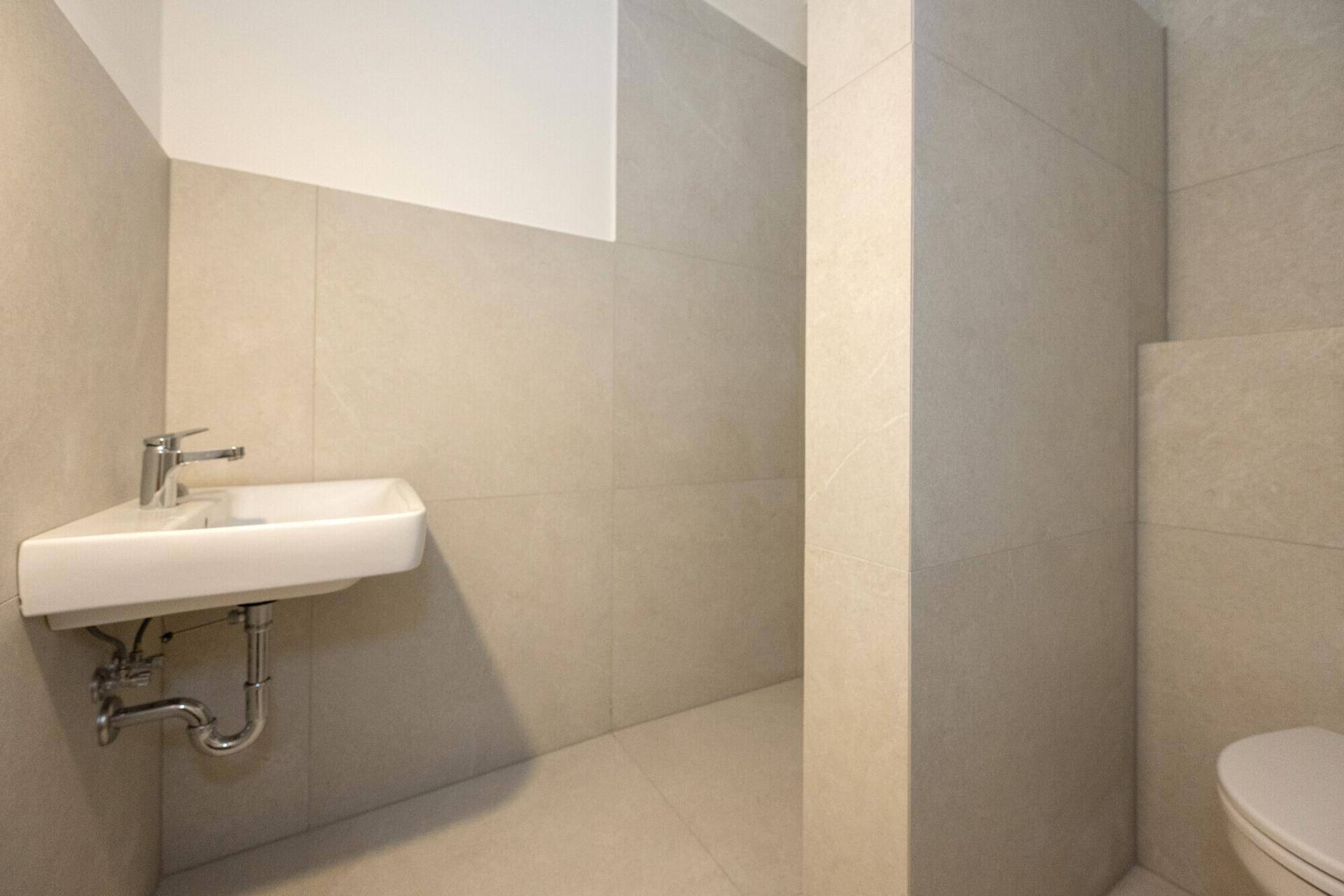 Modernes Badezimmer mit hellem Fliesenboden, Wandwaschbecken und Wand-WC in neutralen Farben.