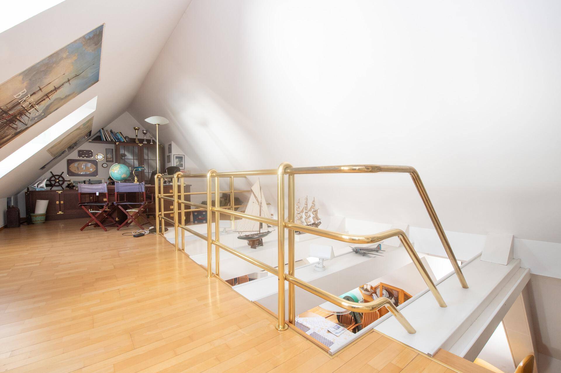 Geräumige Dachgeschossgalerie mit Holzfußboden, Messinggeländer und Blick auf den unteren Wohnbereich.