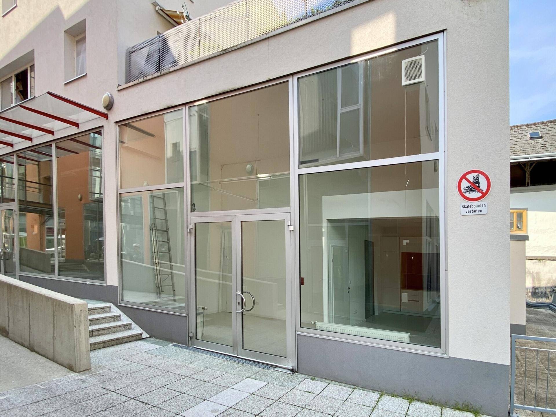 Moderne Geschäftsfassade mit großen Glasfenstern und Eingangstür, die viel Tageslicht hereinlässt.
