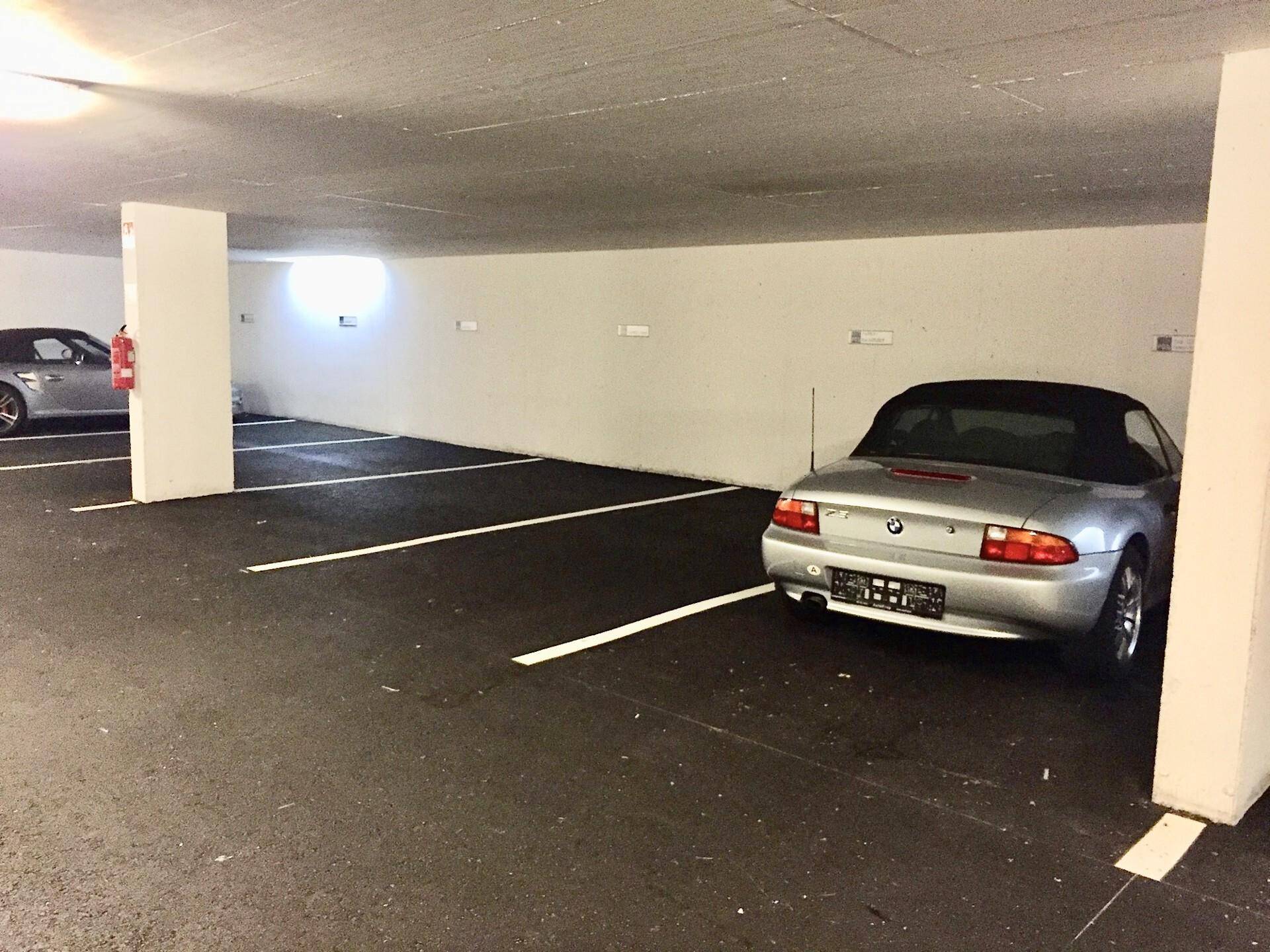 Silberner Roadster parkt auf einem Stellplatz in einer sauberen Tiefgarage mit Feuerlöscher.
