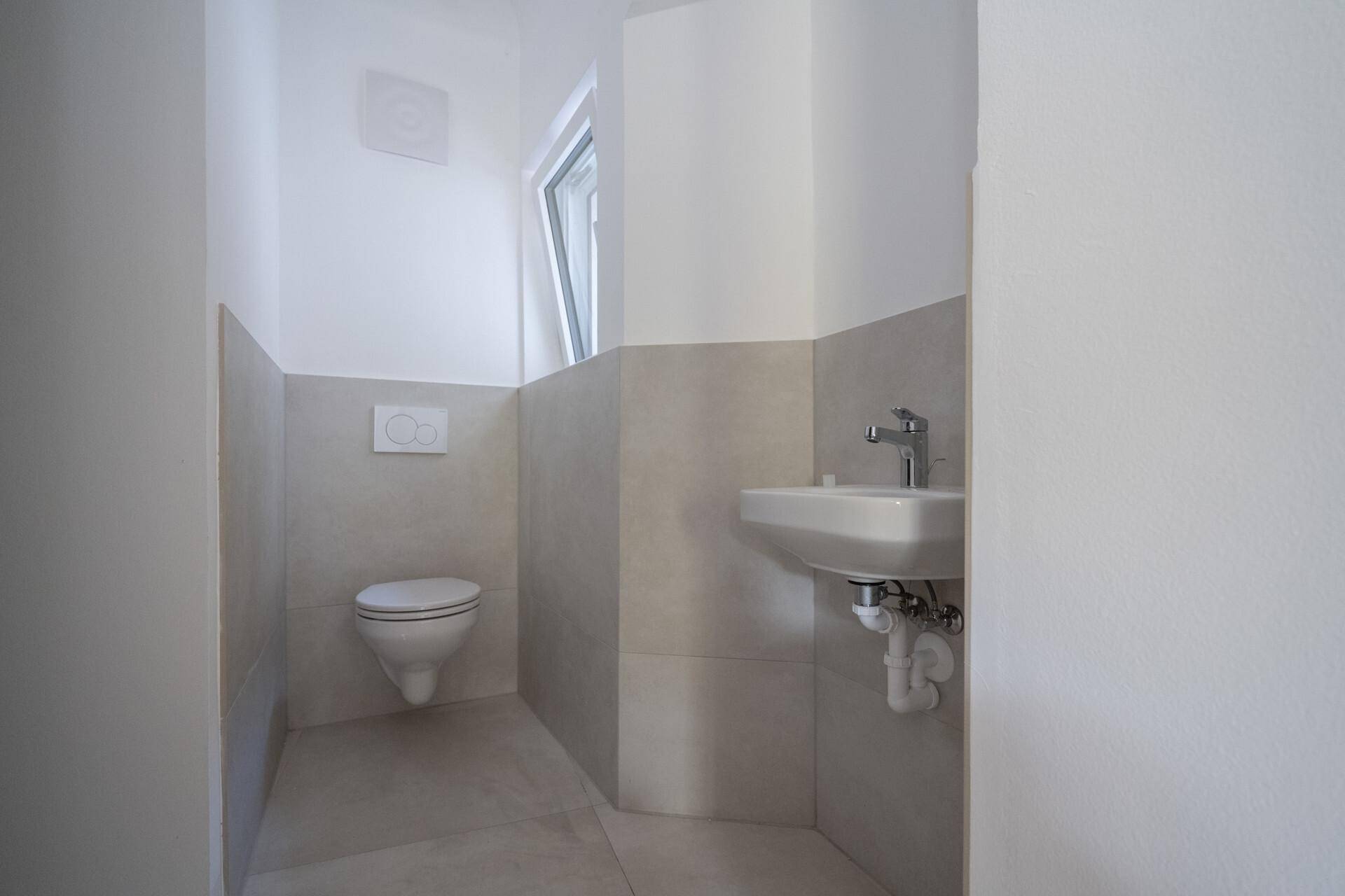 Helles Gäste-WC mit wandhängender Toilette, kleinem Waschbecken und Fenster.
