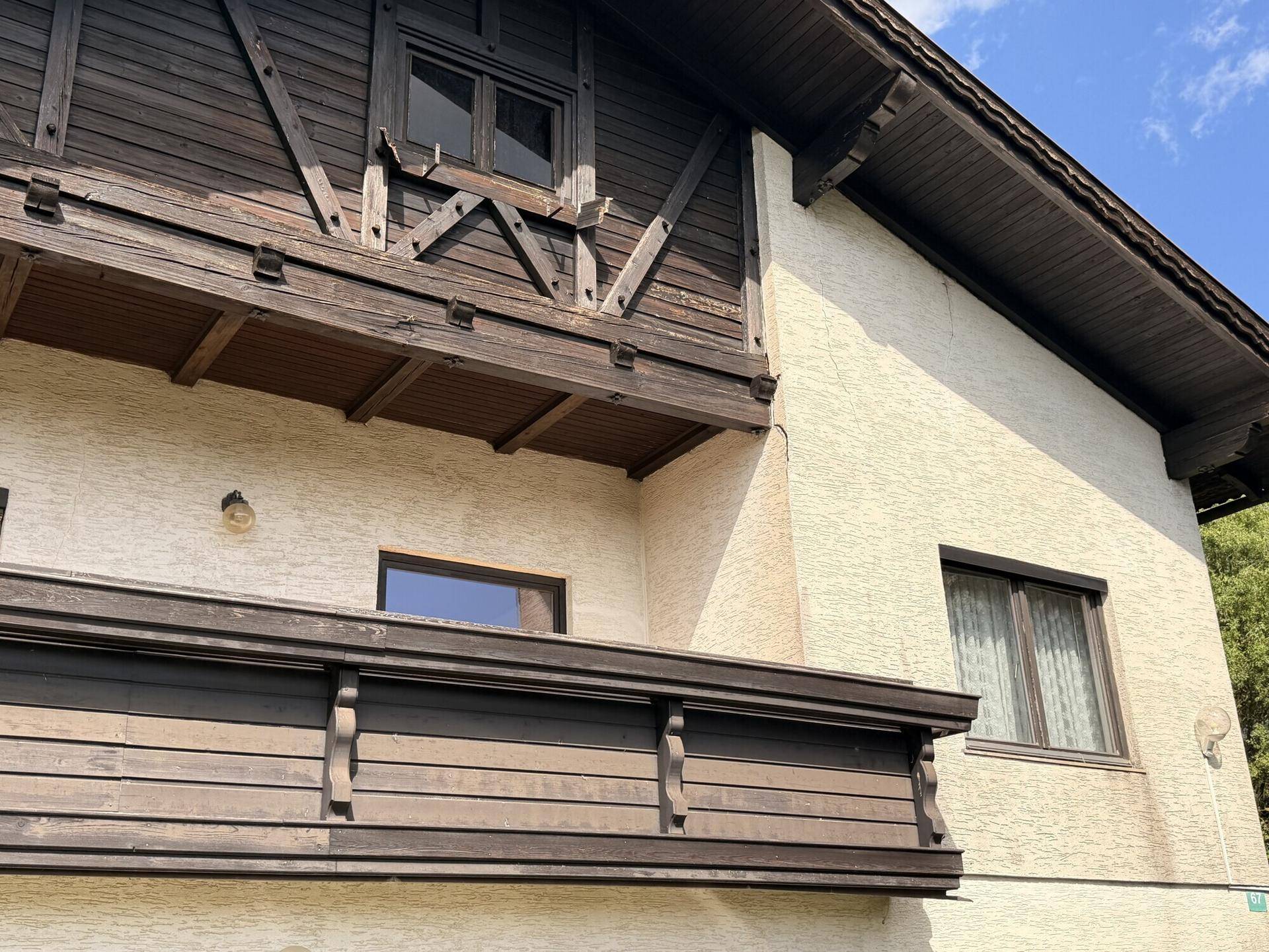 Nahaufnahme der Hausfassade mit traditionellem Holzbalkon und strukturiertem Putz.