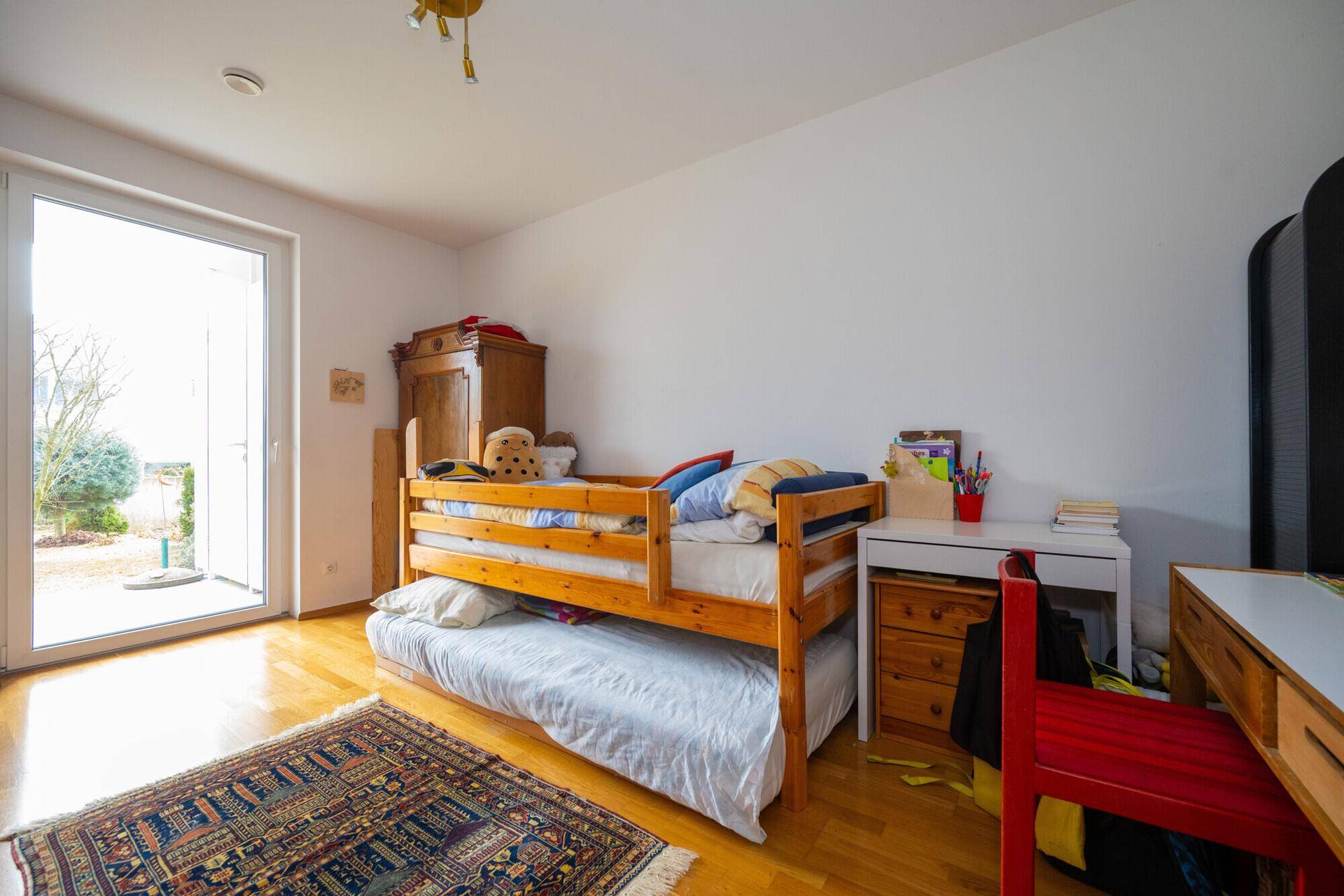 Kinderzimmer mit Etagenbett, Holzboden und Zugang zu einem Außenbereich.