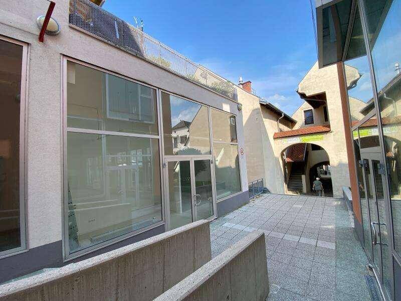 Moderne Geschäftsfassade mit großen Glasfenstern und einem gepflasterten Gehweg in einer städtischen Umgebung.