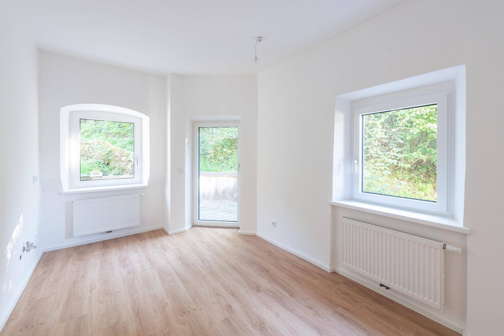 Lichtdurchfluteter Raum mit Laminatboden, weißen Wänden und Zugang zur Terrasse.