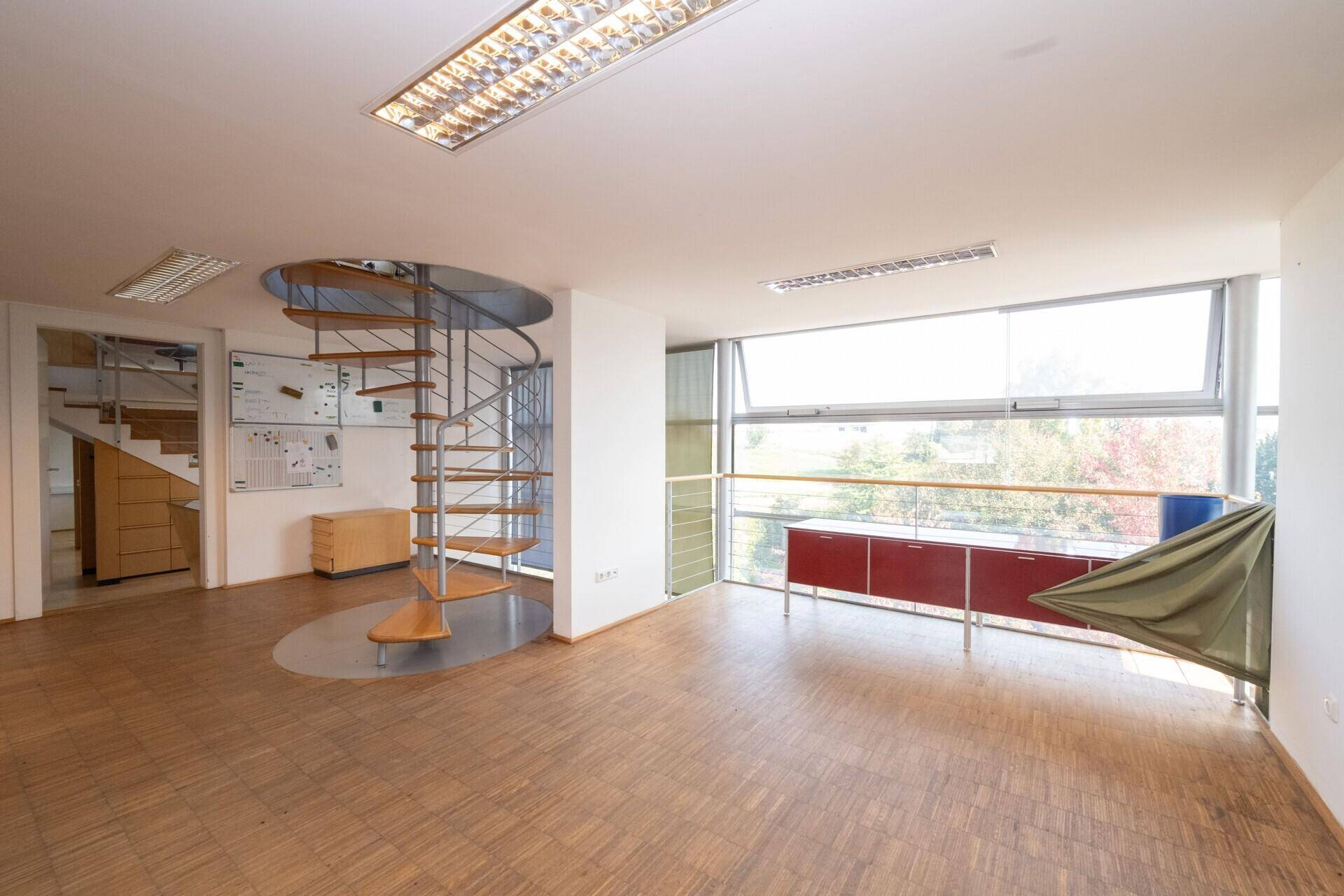 Geräumiges Büro mit Wendeltreppe, großen Fenstern und Holzparkettboden.