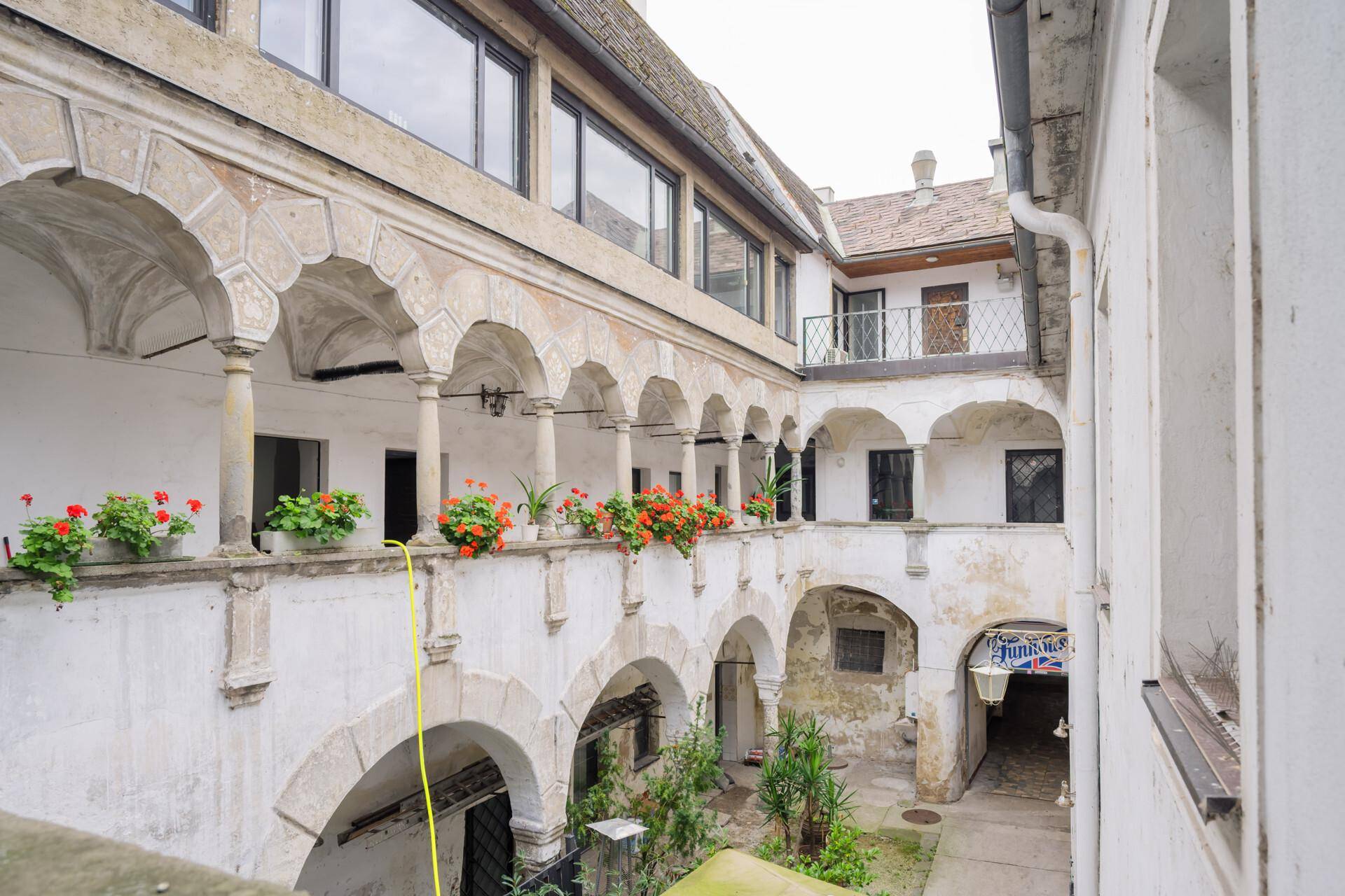 Historischer Innenhof mit Arkaden, Pflanzen und Blumenkästen, der eine ruhige Atmosphäre schafft.