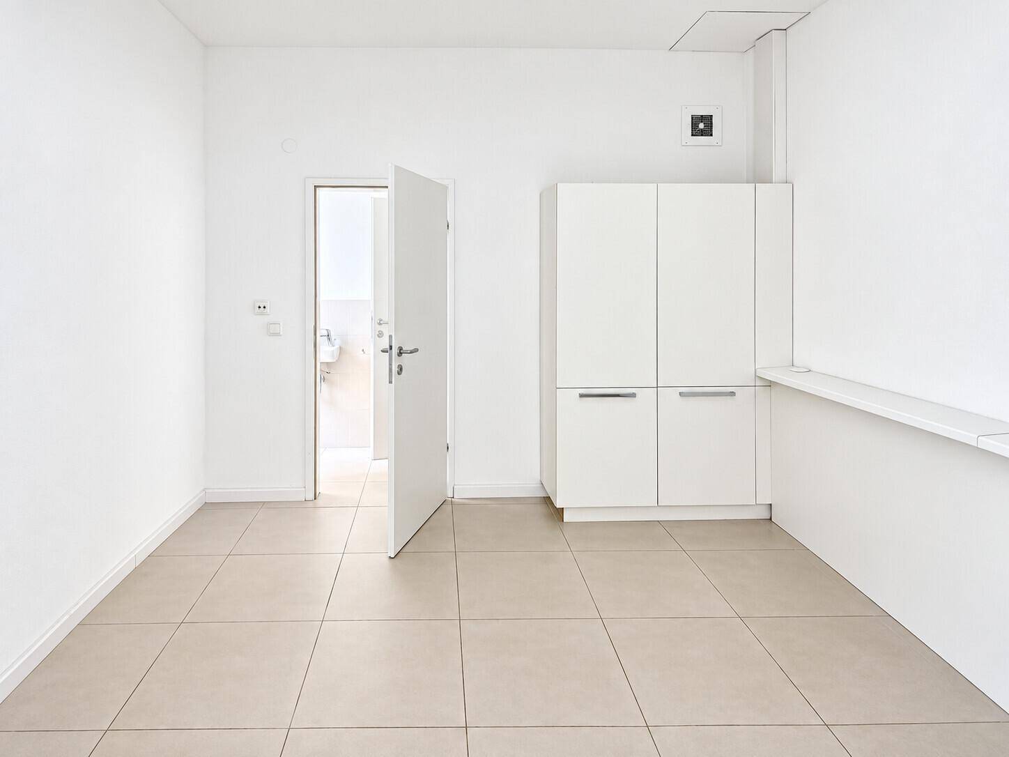 Heller Raum mit weißen Einbauschränken und Zugang zu einem Badezimmer, ideal als Büro.
