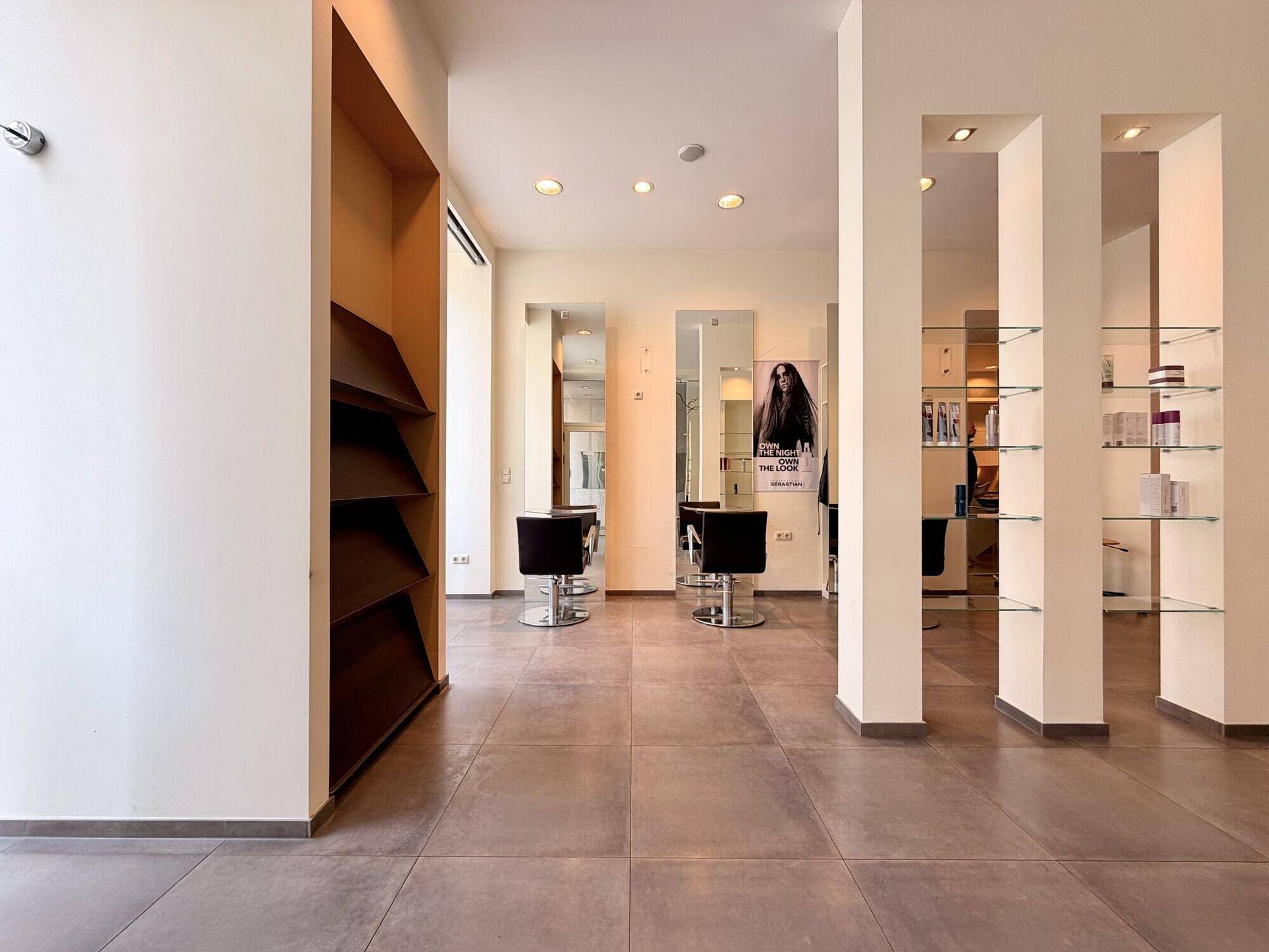 Geräumiger Friseursalon mit großen Schaufenstern, Regalen und modernen Frisierstühlen.