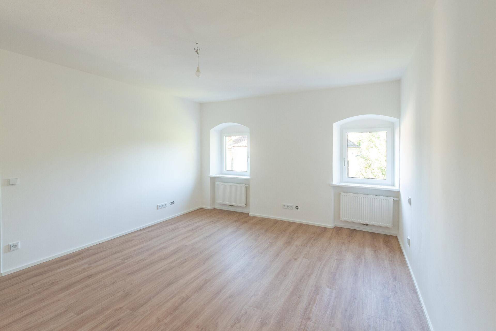 Geräumiger, heller Raum mit Laminatboden und zwei Fenstern, ideal für Wohn- oder Schlafzimmer.