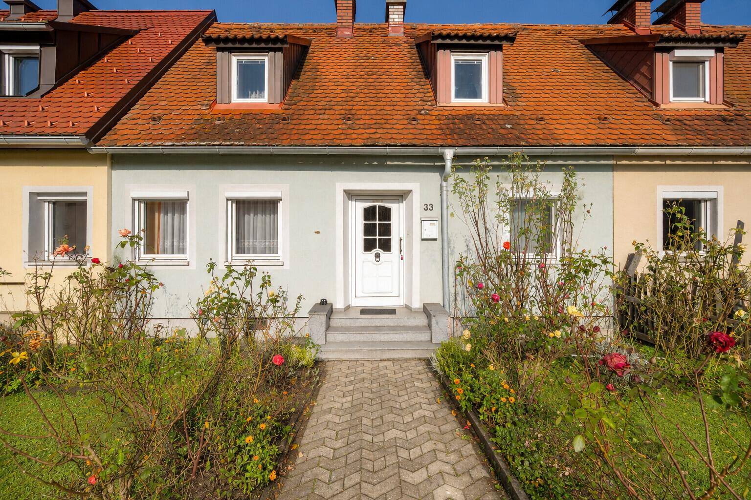 Frontansicht eines Reihenhauses mit weißer Eingangstür und blühendem Vorgarten.