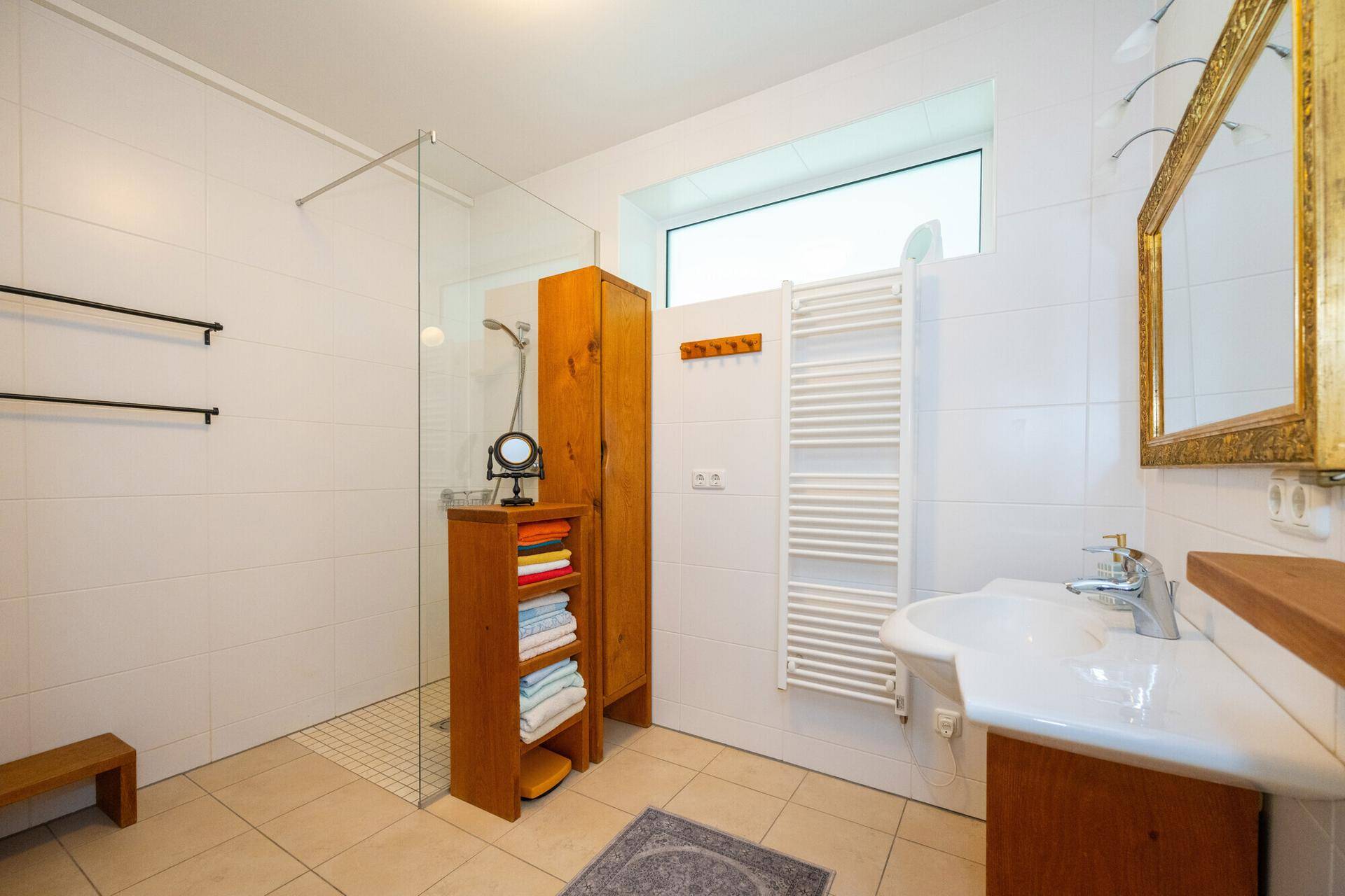 Helles Badezimmer mit weiß gefliesten Wänden, Dusche und Fenster für Tageslicht.