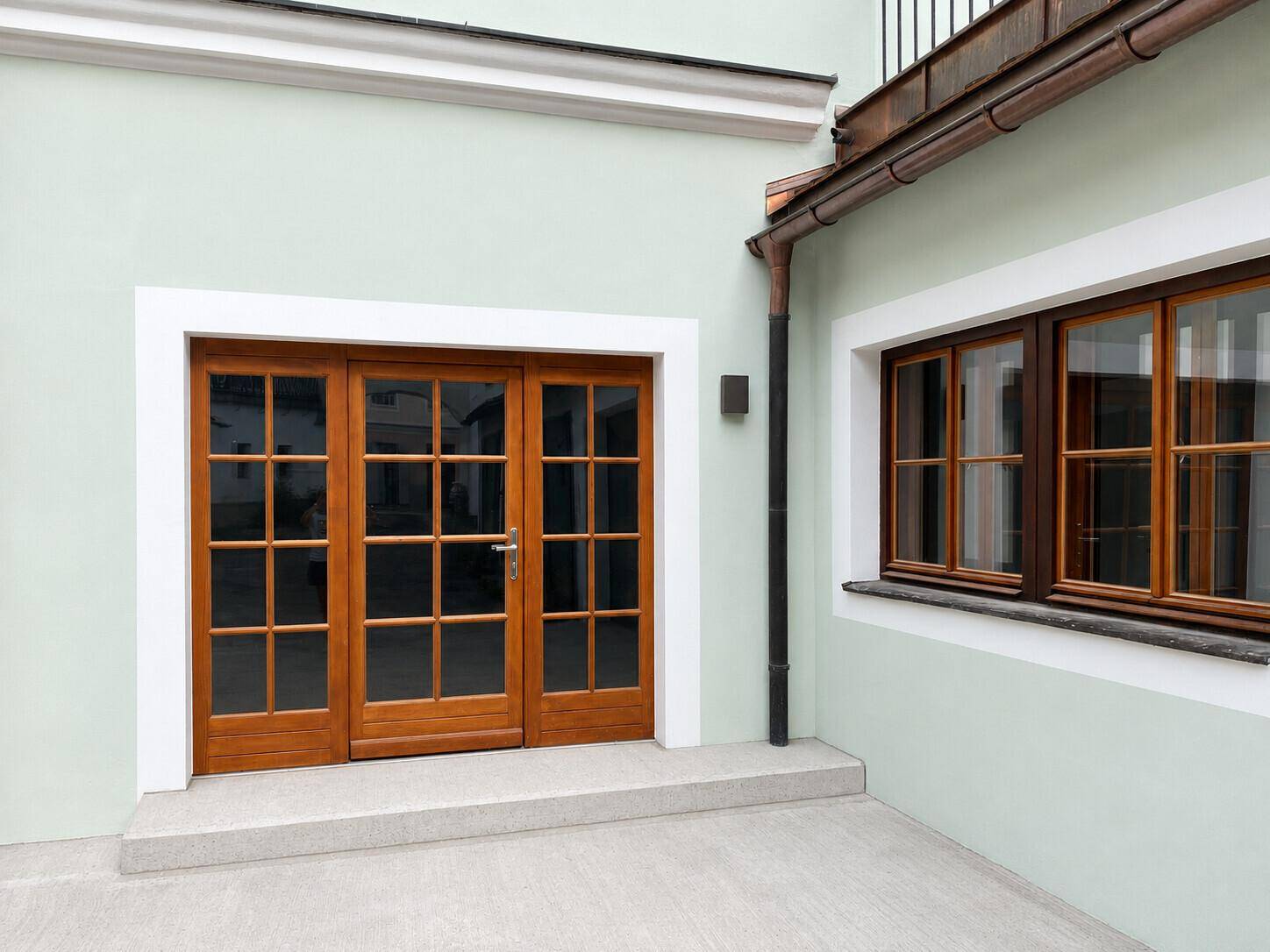 Moderne Hausfassade in hellem Grün mit eleganten Holzfenstern und -türen.