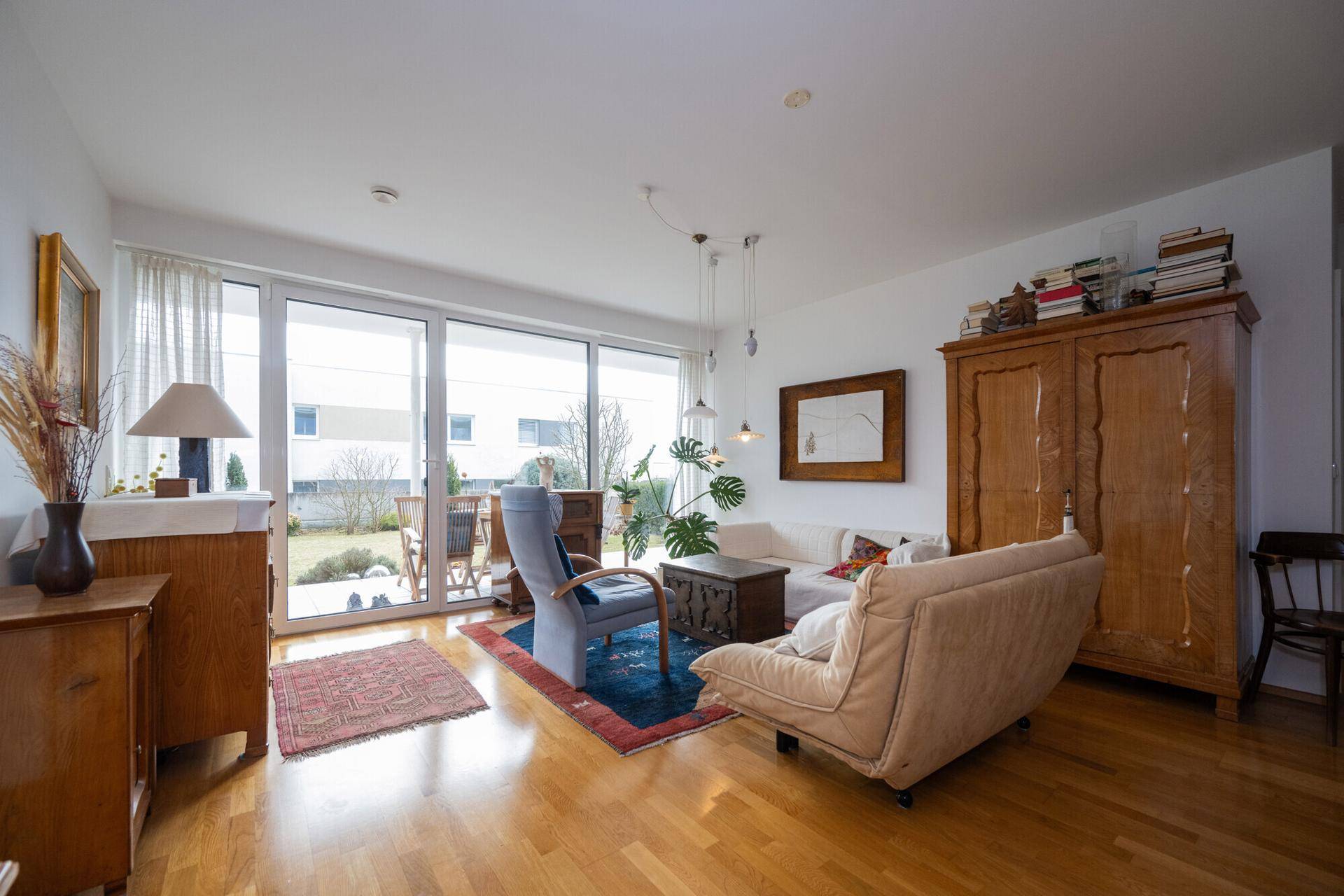 Gemütliches Wohnzimmer mit Holzboden, großen Fenstern und Zugang zum Garten.