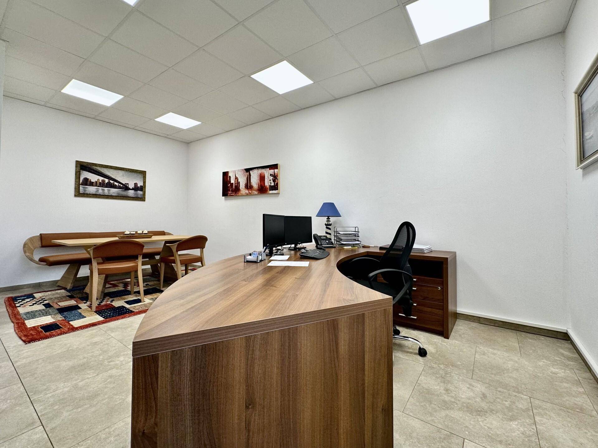 Büro mit einem großen Holzschreibtisch und einem Essbereich mit Bank und Stühlen im Hintergrund.