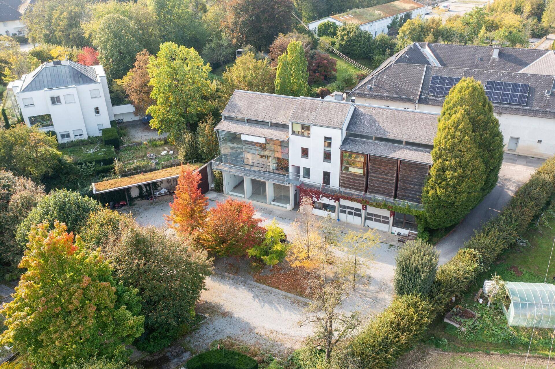 Luftaufnahme des Anwesens mit moderner Architektur, umgeben von üppiger Vegetation und herbstlichen Bäumen.