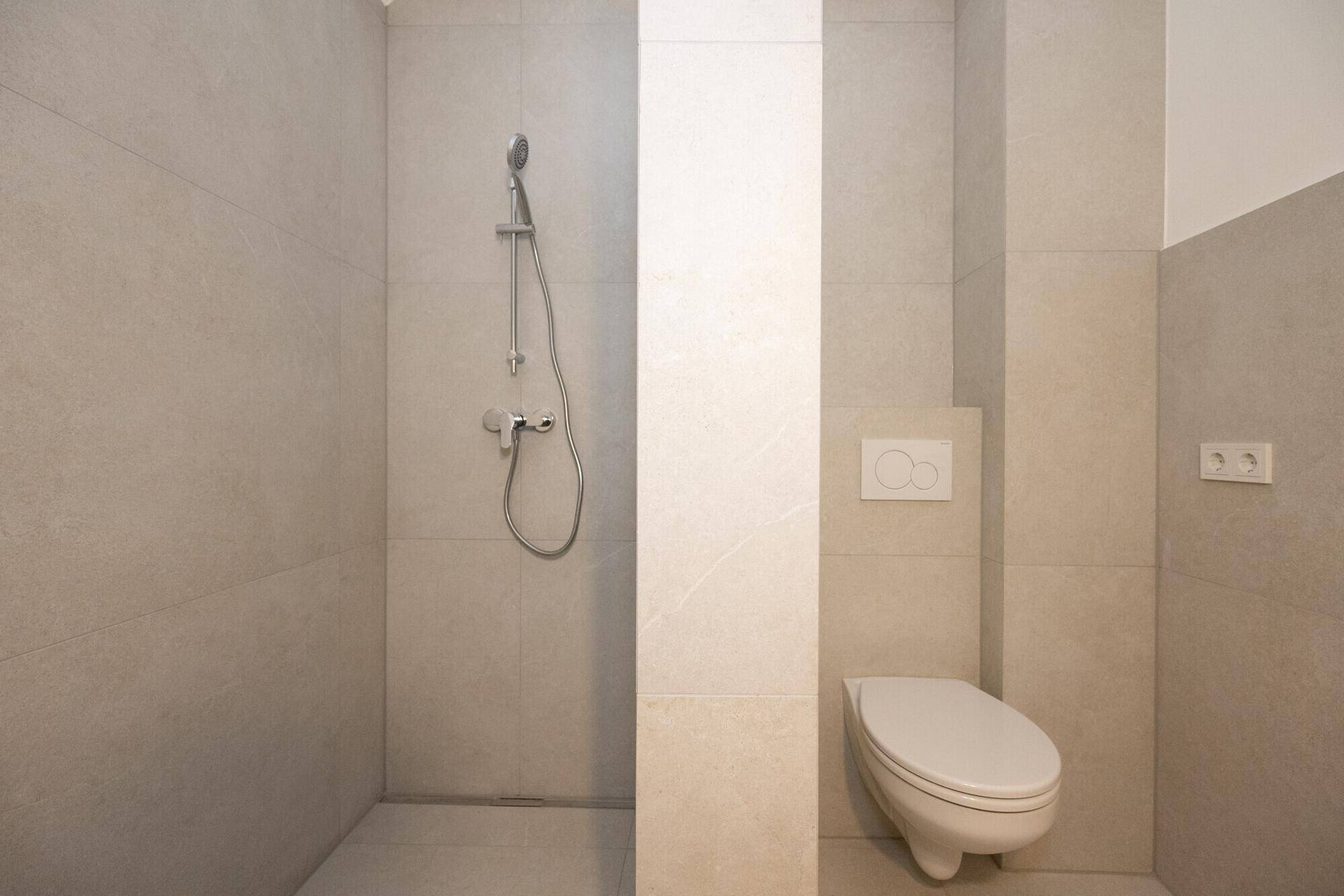 Modernes Badezimmer mit Duschbereich, Wand-WC und hellen Fliesen, frisch renoviert und funktional.