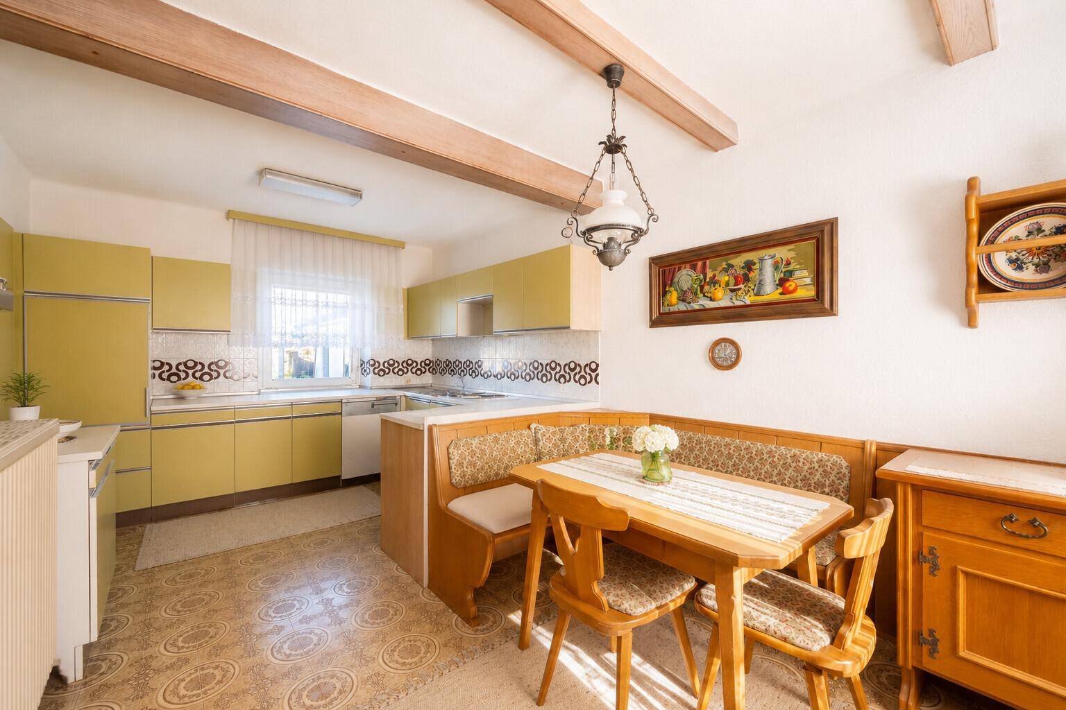 Traditionelle Wohnküche mit gelben Schränken, Essbereich und sichtbaren Holzbalken an der Decke.