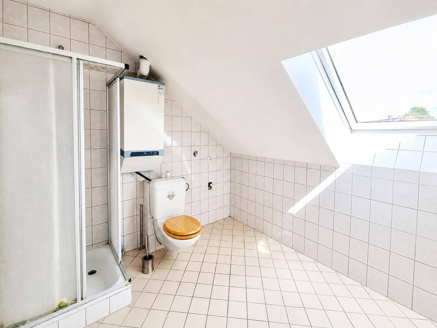 Gefliestes Badezimmer im Dachgeschoss mit Dusche, WC und Dachfenster.