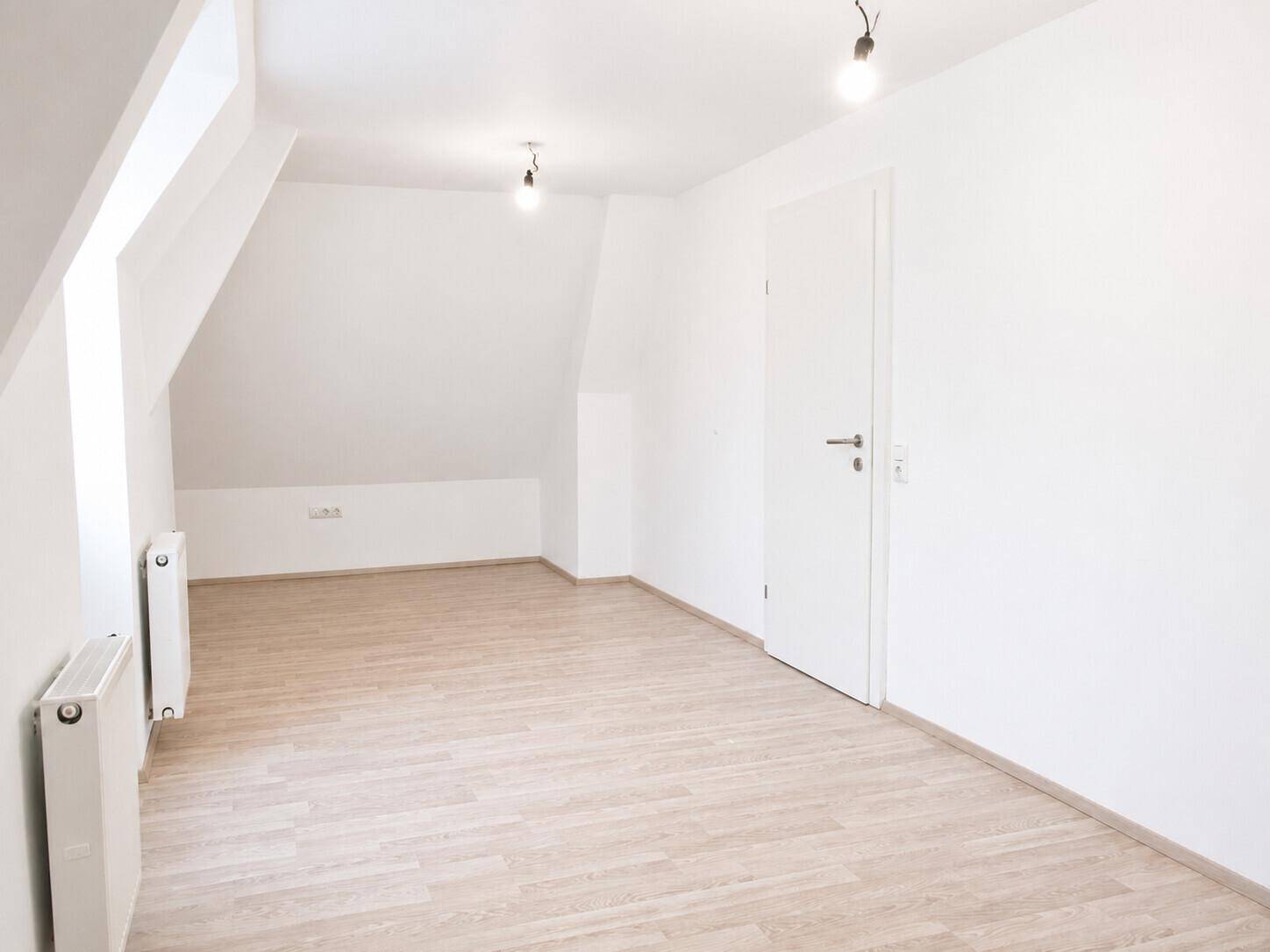 Großer, heller Raum mit Laminatboden und Dachschrägen, ideal als Schlaf- oder Wohnzimmer.