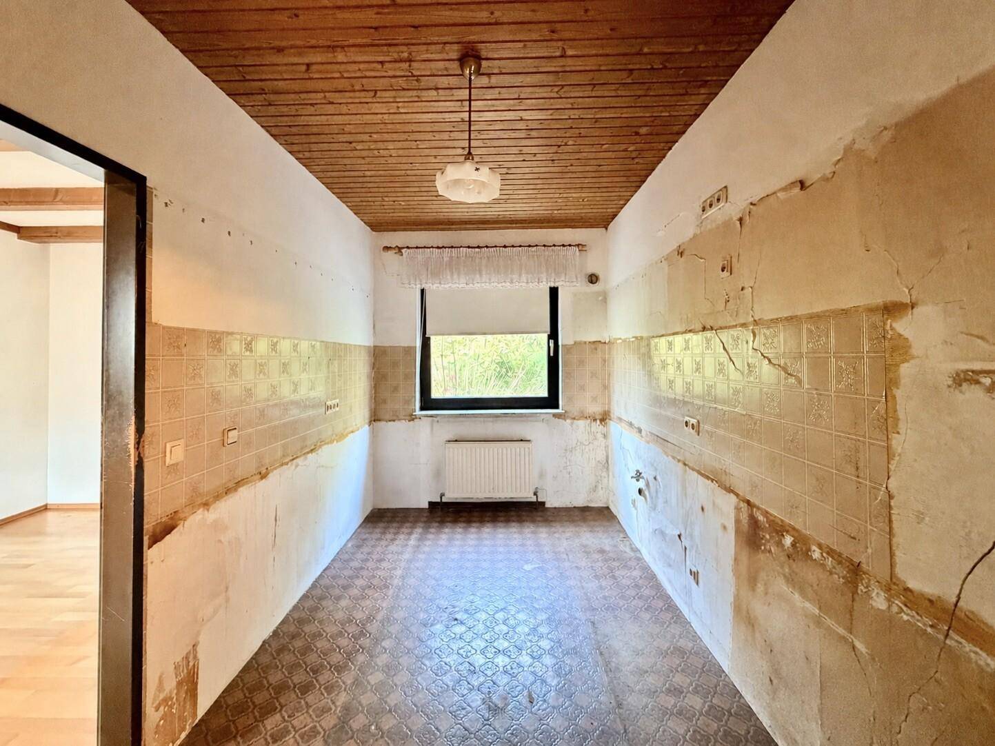 Renovierungsbedürftige Küche mit alten Fliesen und Fenster, bereit für eine Neugestaltung.