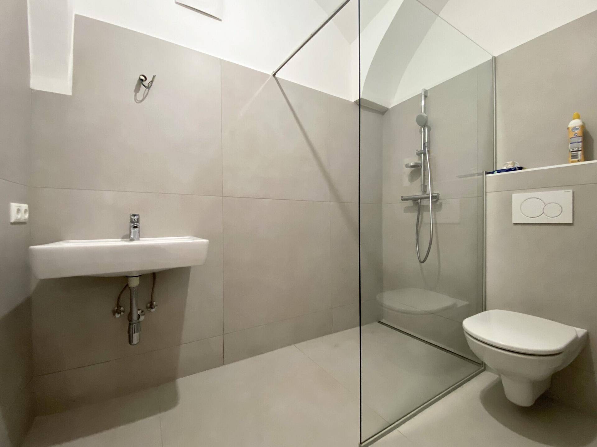 Modernes Badezimmer mit begehbarer Dusche, Wand-WC und hellem Fliesenboden.