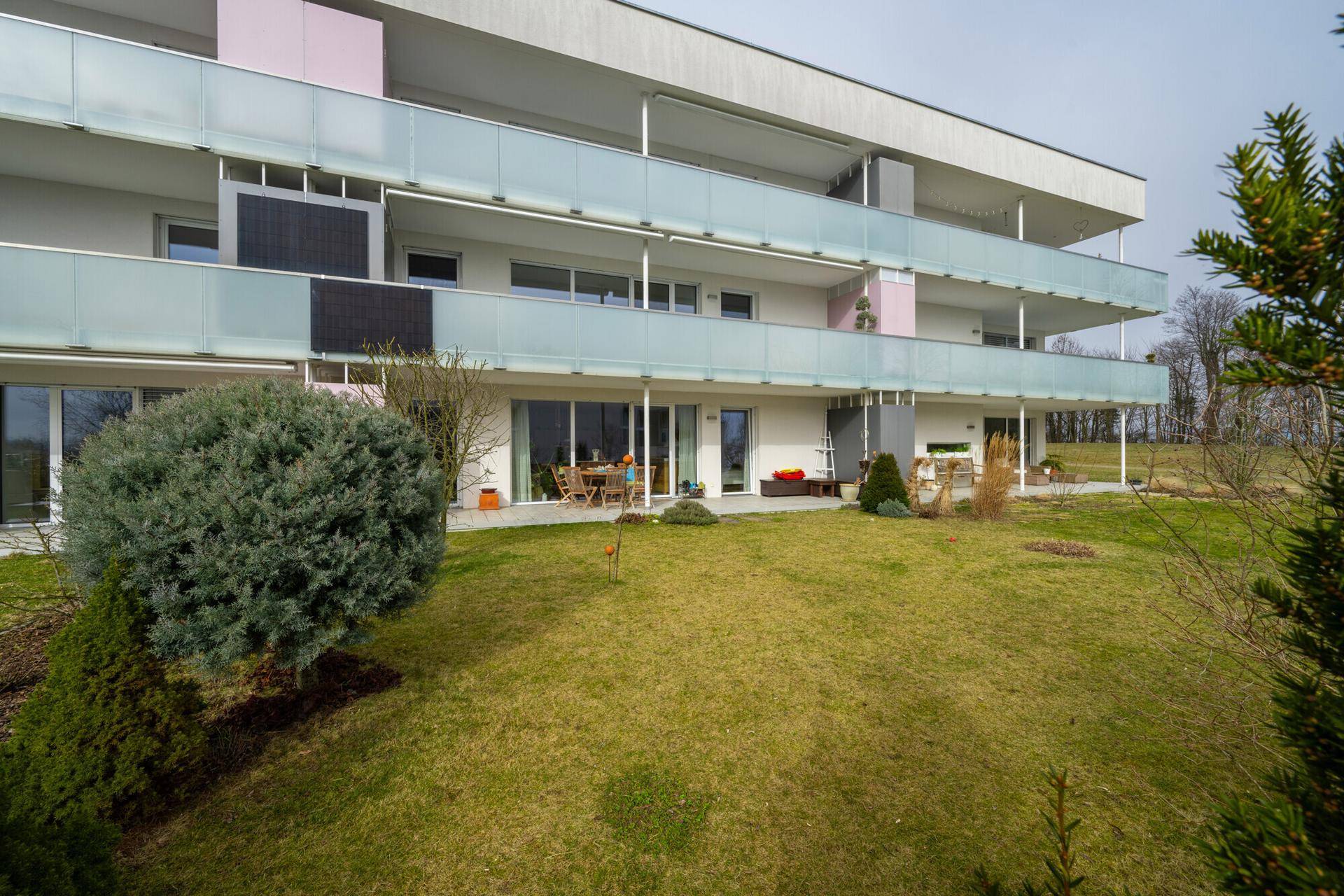 Weitläufiger Gartenbereich mit Rasen und Sträuchern, angrenzend an die Terrassen der Wohnungen.