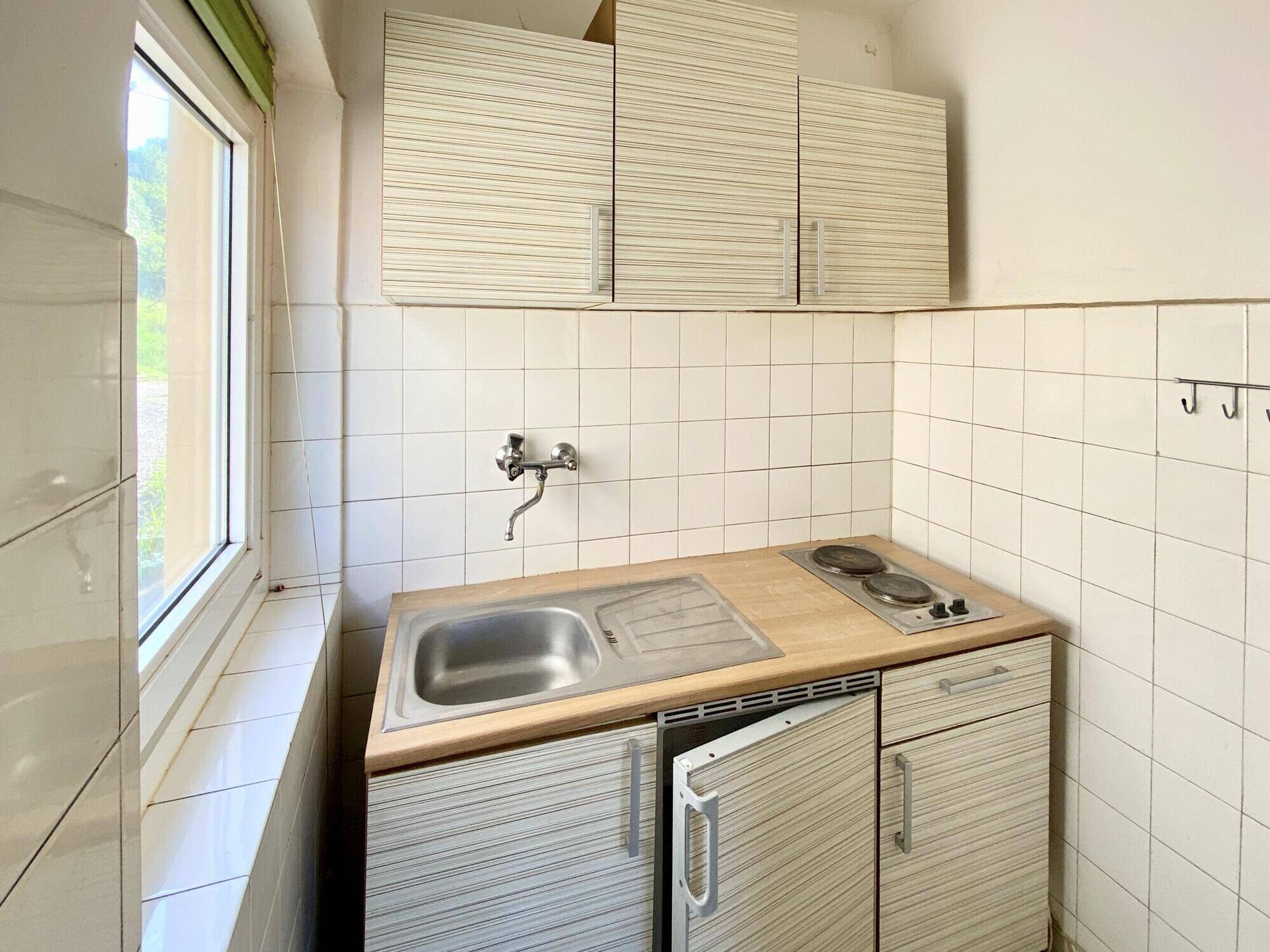 Kleine Küchenzeile mit Spüle, Kochplatten und Oberschränken in einem hellen Raum.