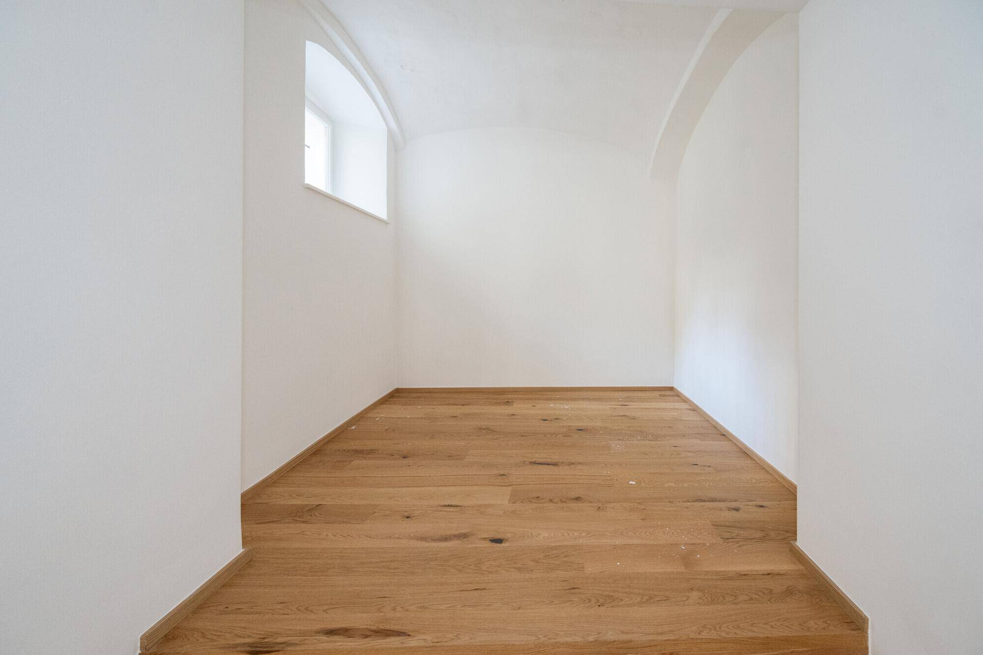 Kleiner, heller Raum mit Holzboden und einer eleganten Gewölbedecke, ideal als Rückzugsort.