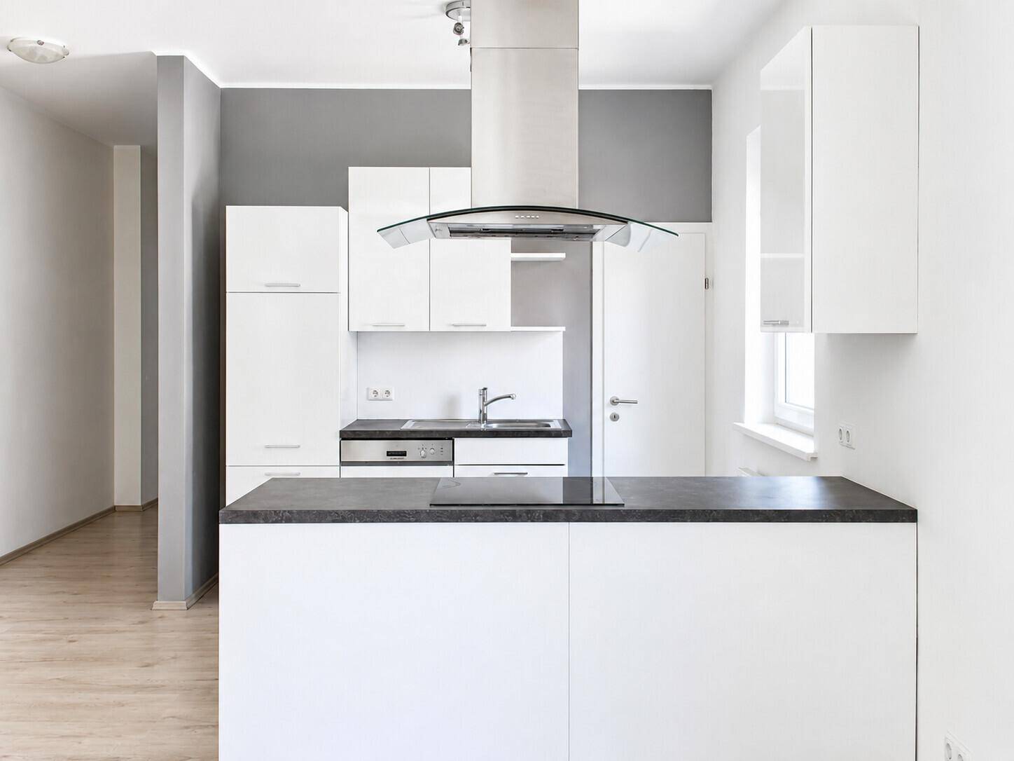 Moderne Einbauküche mit weißen Fronten, dunkler Arbeitsplatte und integrierten Geräten in einem hellen Raum.