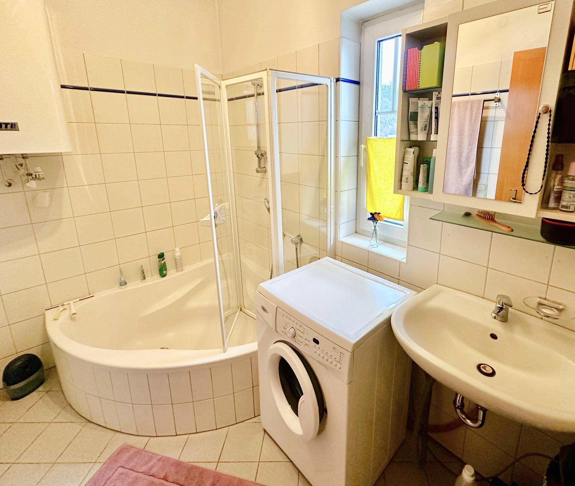 Badezimmer mit Eckbadewanne, Dusche, Waschbecken und Waschmaschine.