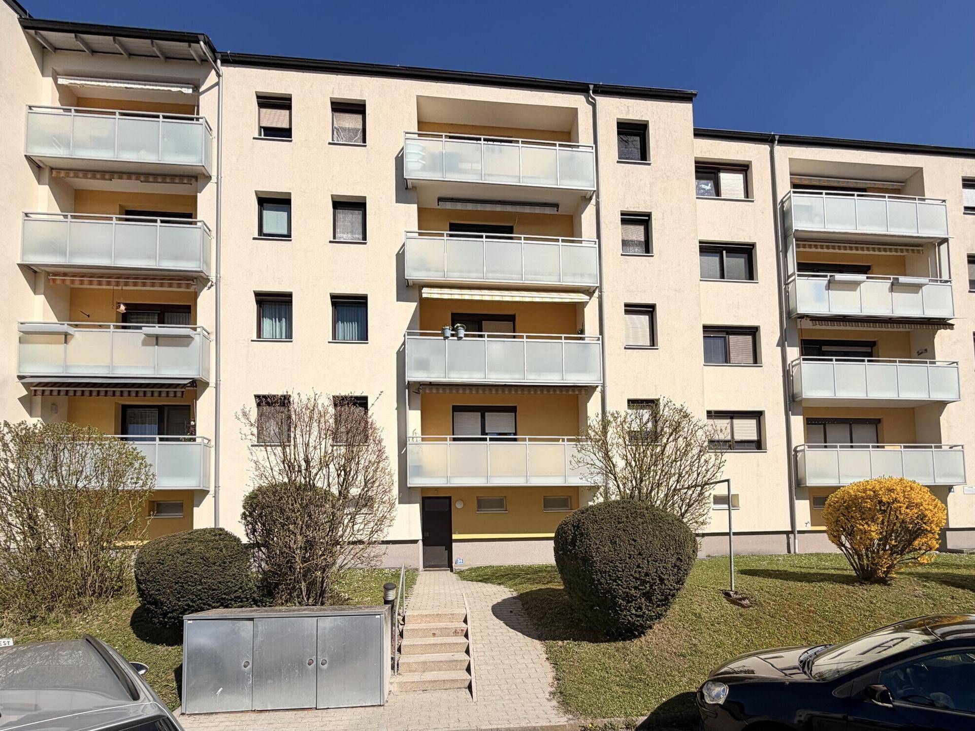 Mehrfamilienhaus mit gelber Fassade und zahlreichen Balkonen in einer städtischen Umgebung.