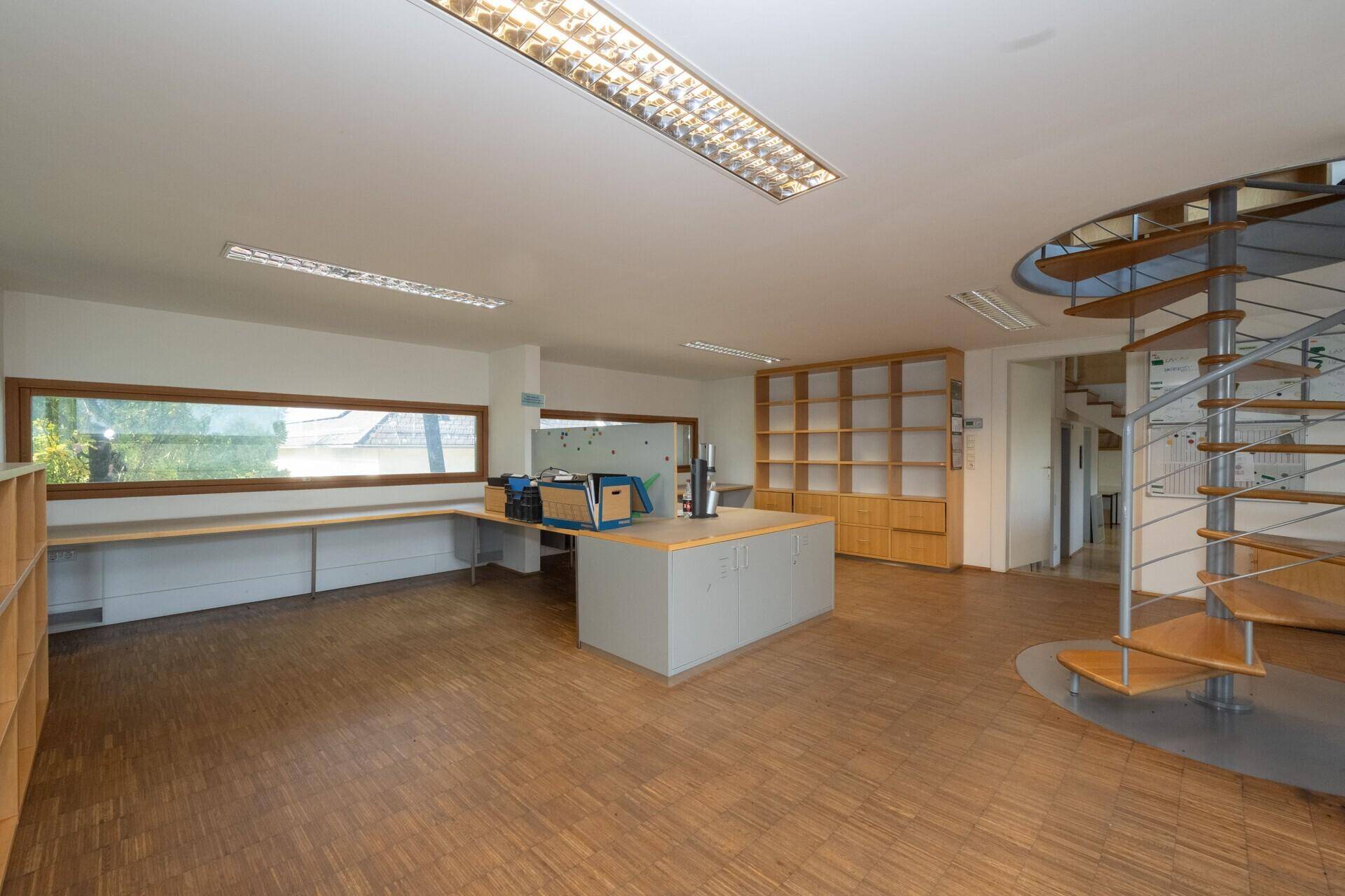 Großes Büro mit Holzparkett, eingebauten Regalen und einem zentralen Arbeitstisch.