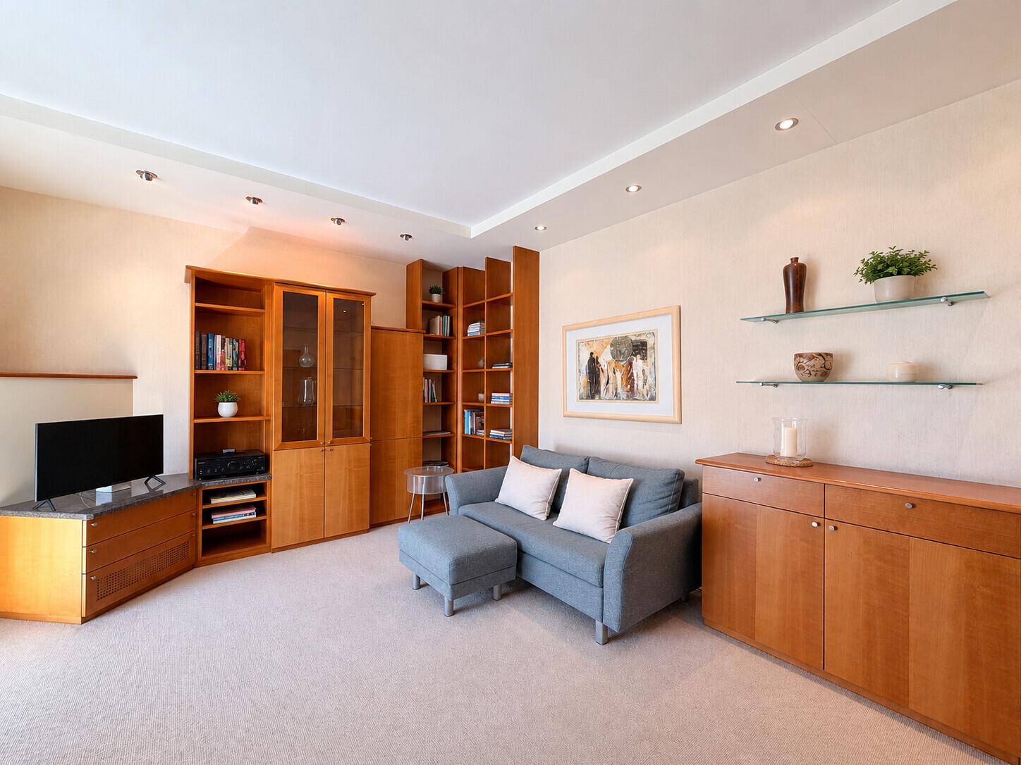 Wohnzimmer mit beigem Teppichboden, bequemer Couch und umfangreichen Holzmöbeln für Stauraum.