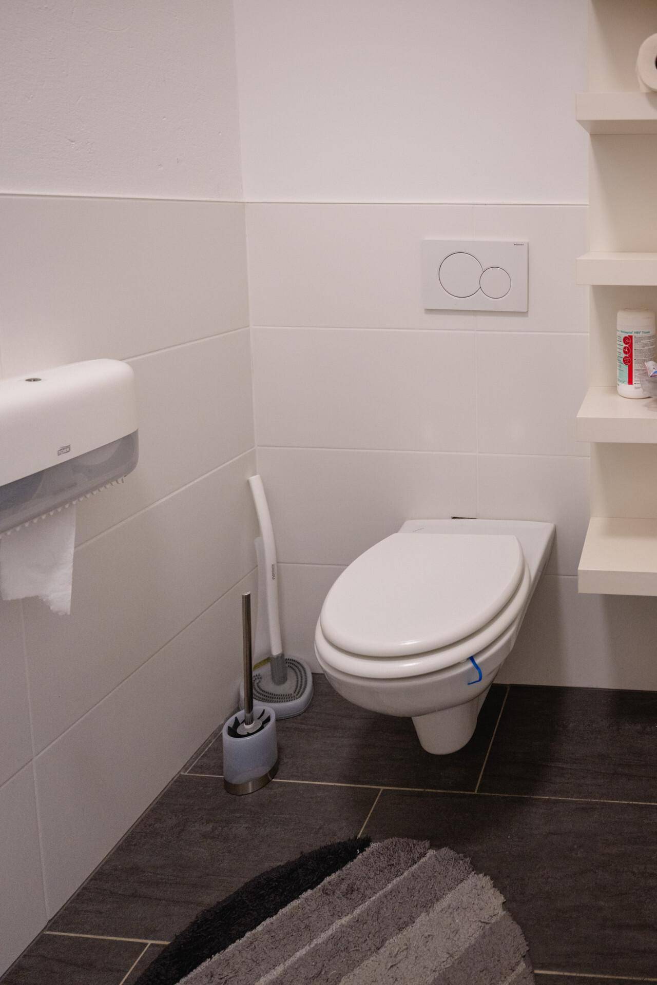 Modernes WC mit wandhängender Toilette, dunklen Bodenfliesen und weißen Wandfliesen.