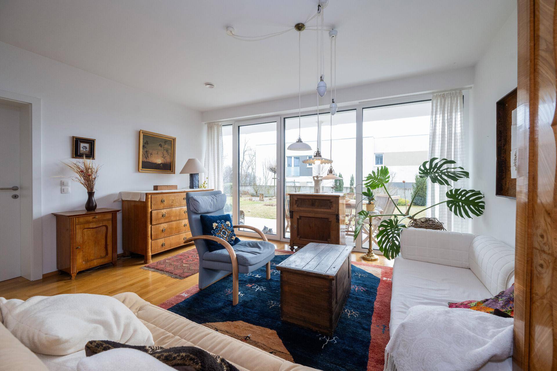 Lichtdurchflutetes Wohnzimmer mit großen Fenstern, Holzboden und Blick ins Grüne.