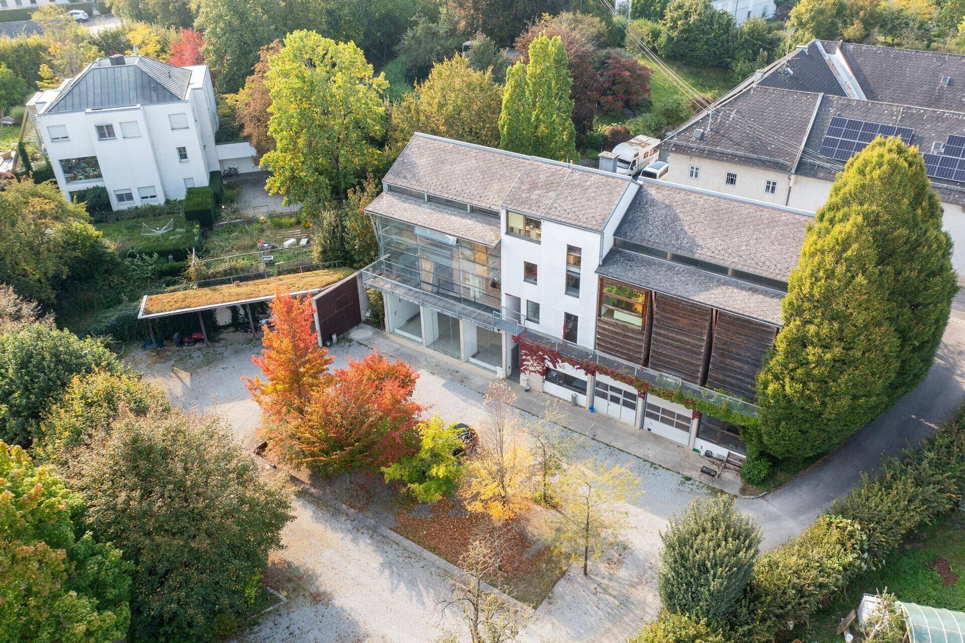 Luftaufnahme des Gebäudes mit moderner Fassade, umgeben von Bäumen in Herbstfarben und Parkplätzen.