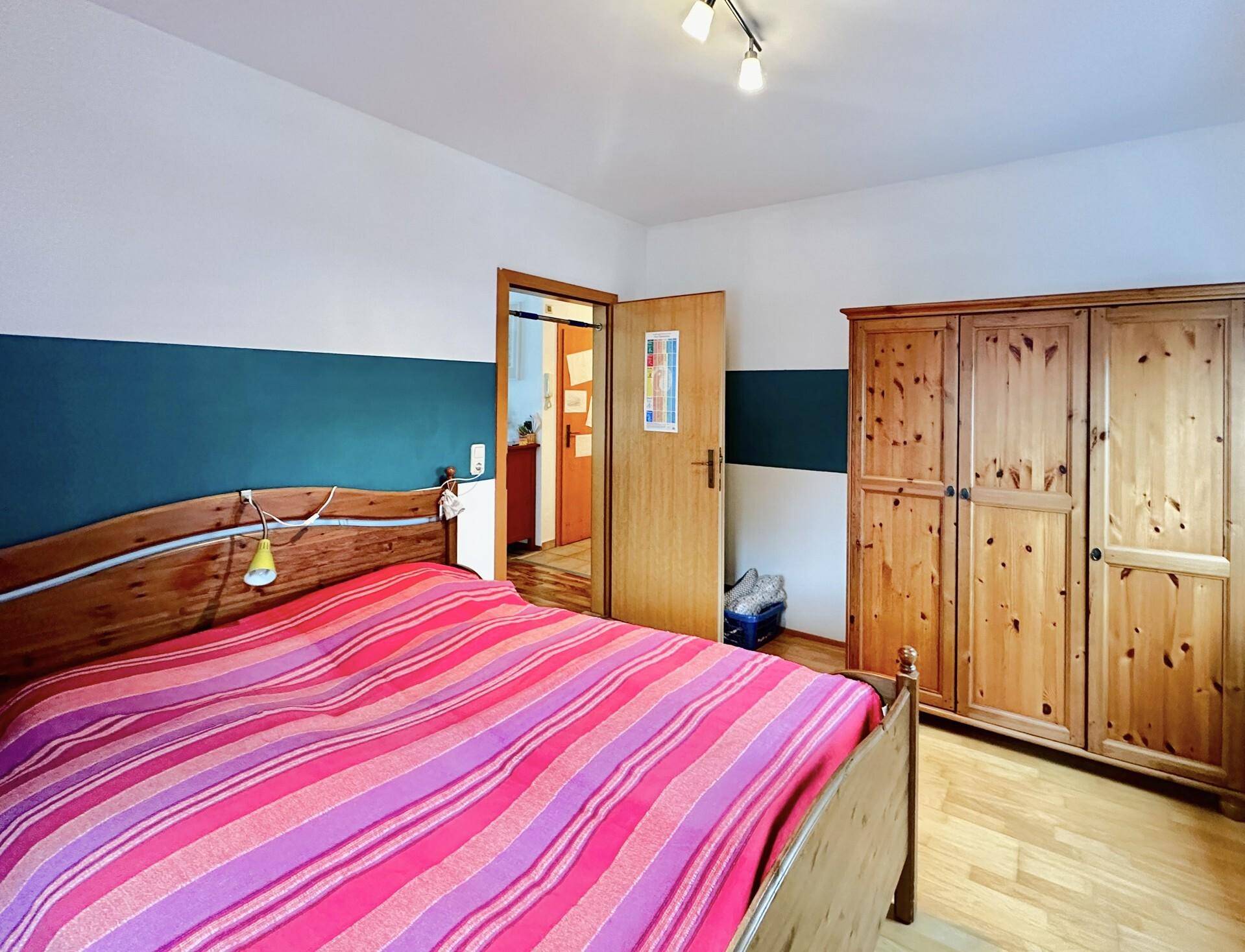 Schlafzimmer mit Holzbett, Kleiderschrank und farbiger Wandgestaltung.